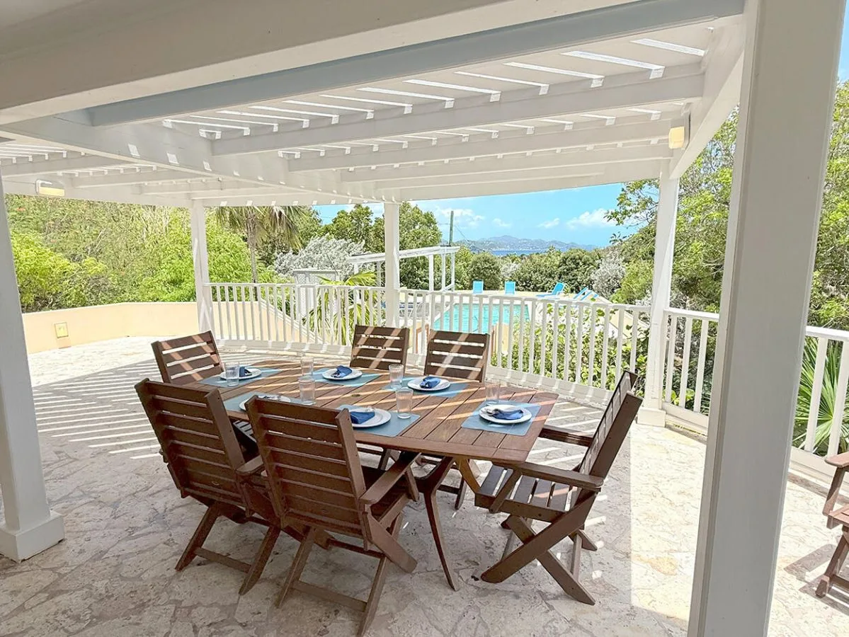 An outdoor dining area sits beneath a covered patio, with a table set for a meal.