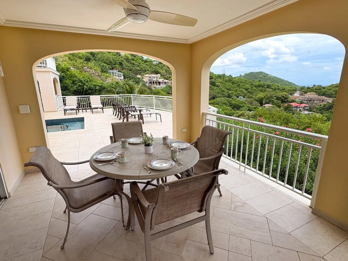 Una terraza cubierta con mesa de comedor ofrece vistas a colinas verdes y una piscina.