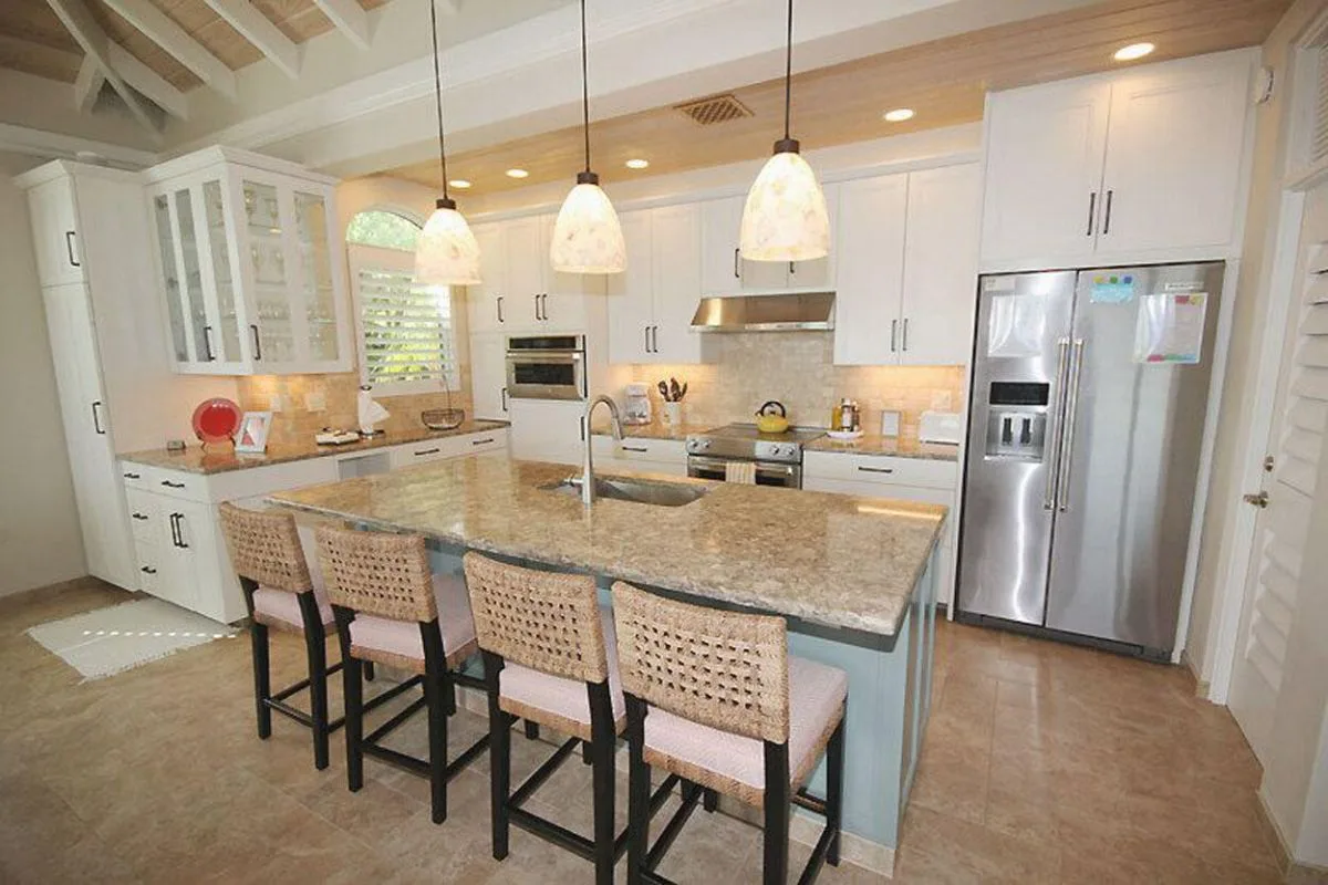 Una cocina luminosa con una isla grande, luces colgantes y gabinetes blancos.