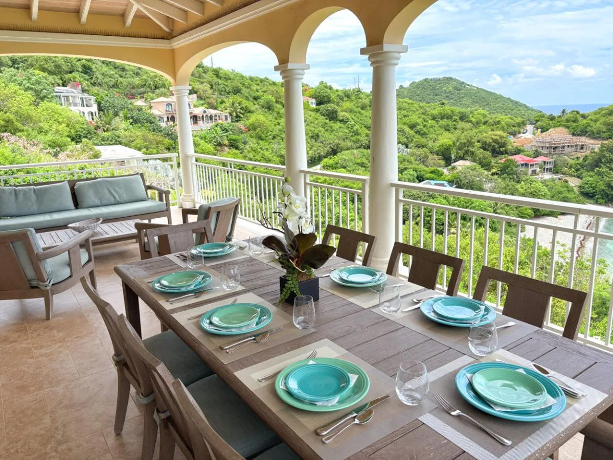 Comedor exterior cubierto con la mesa puesta y vistas a colinas verdes.