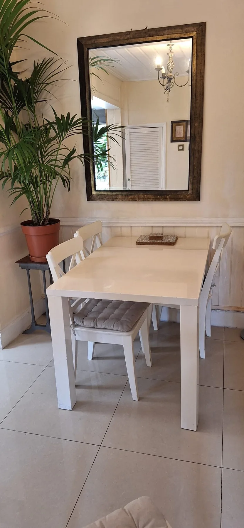 A dining area with a white table, chairs, and a large wall mirror.