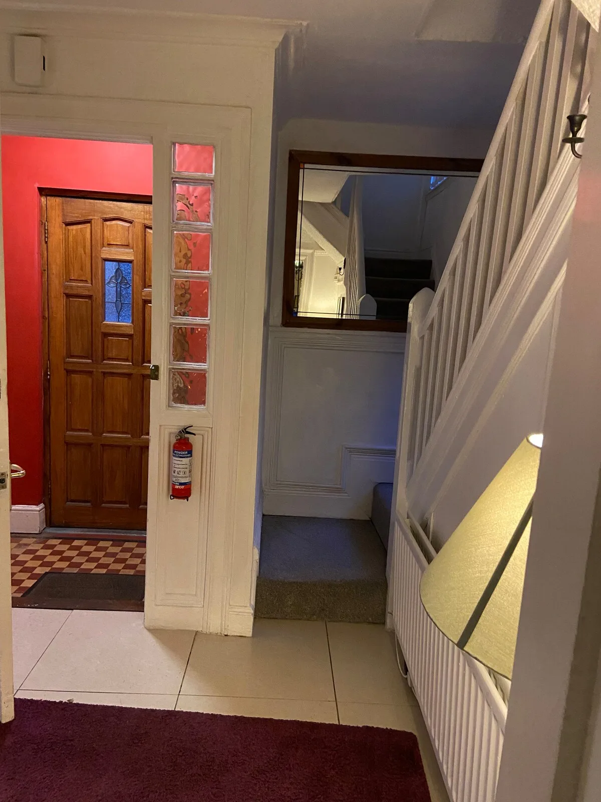 An interior hallway with a wooden entrance door, staircase, and floor lamp.