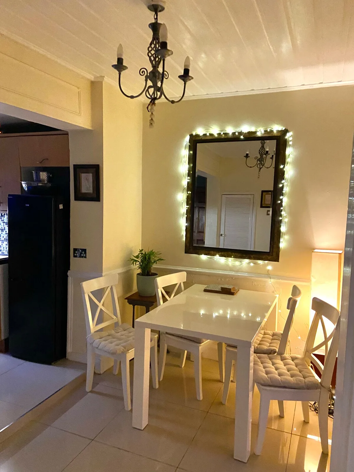 Dining area with a white table, chairs, and a lighted wall mirror.