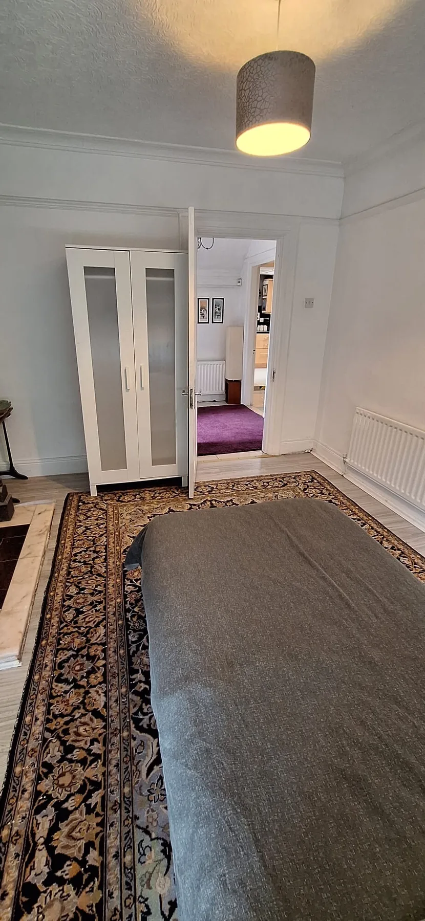 A bedroom with a bed, patterned rug, and wardrobe beside an open doorway.