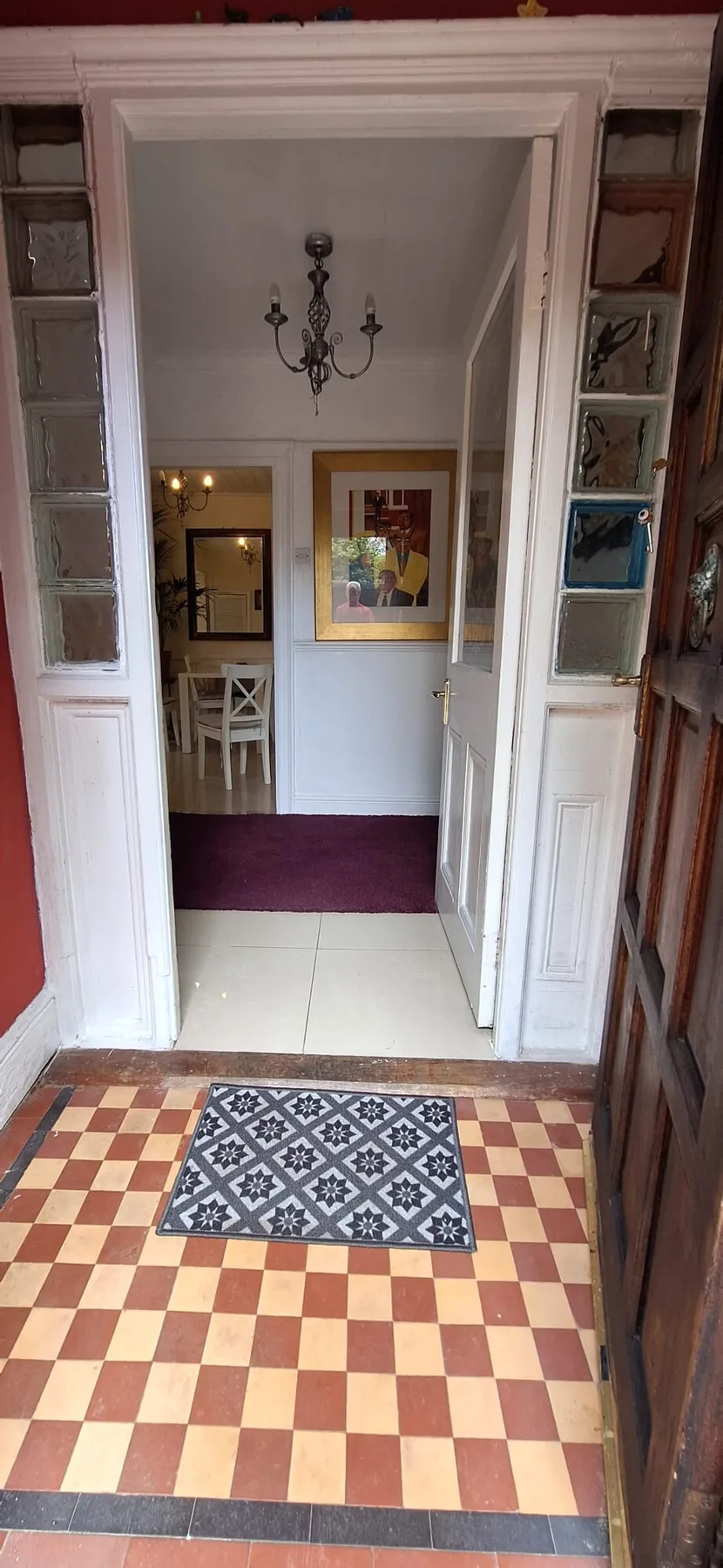 An interior doorway opens onto a tiled hall with a patterned rug and chandelier.