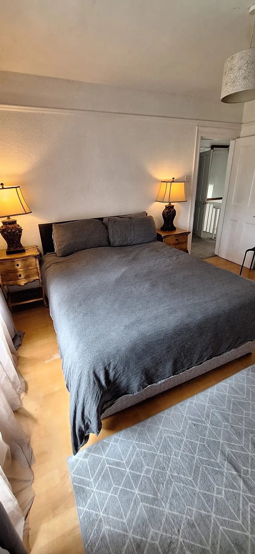 A bedroom with a large bed, bedside tables, and a patterned rug.