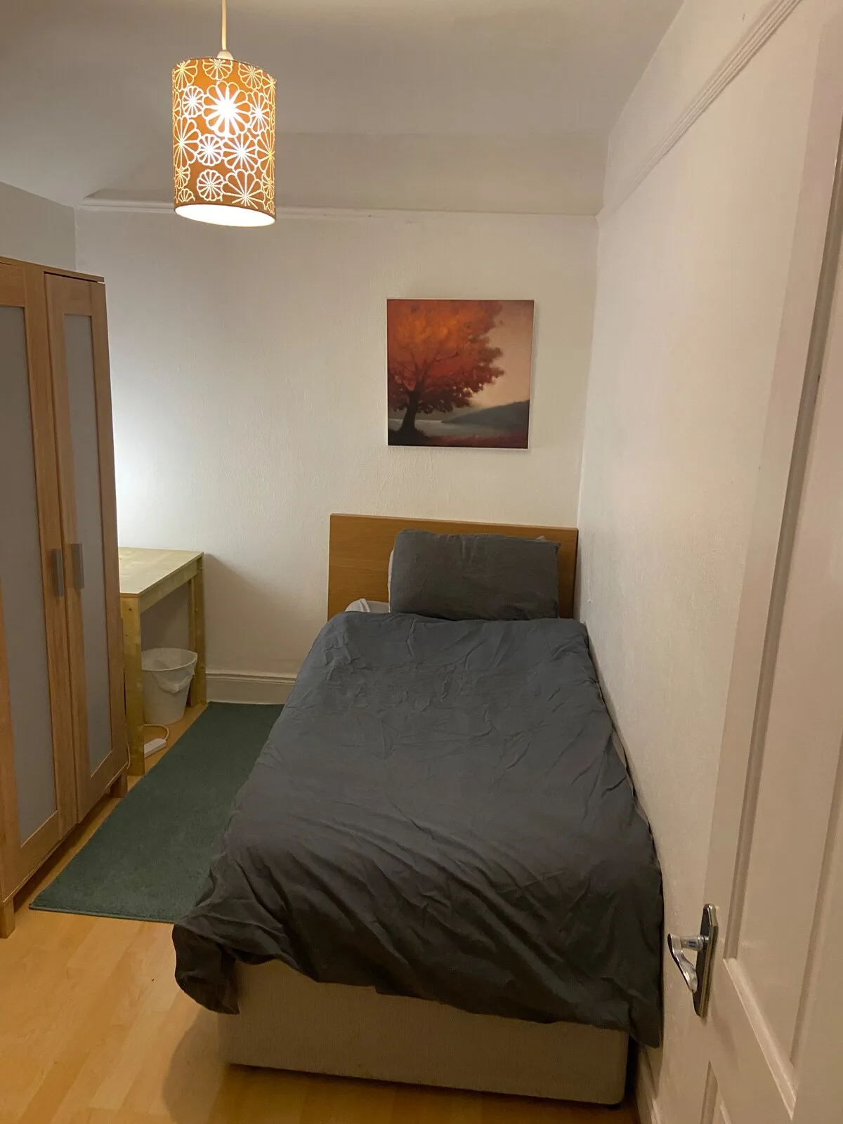 A bedroom with a bed covered in gray bedding and a framed picture on the wall.