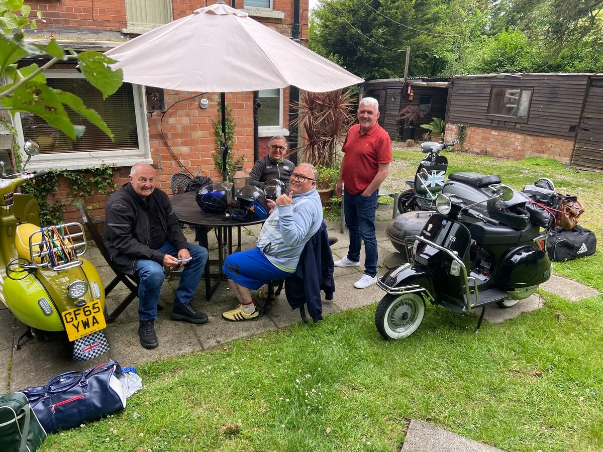 A garden seating area with people gathered beside parked scooters.