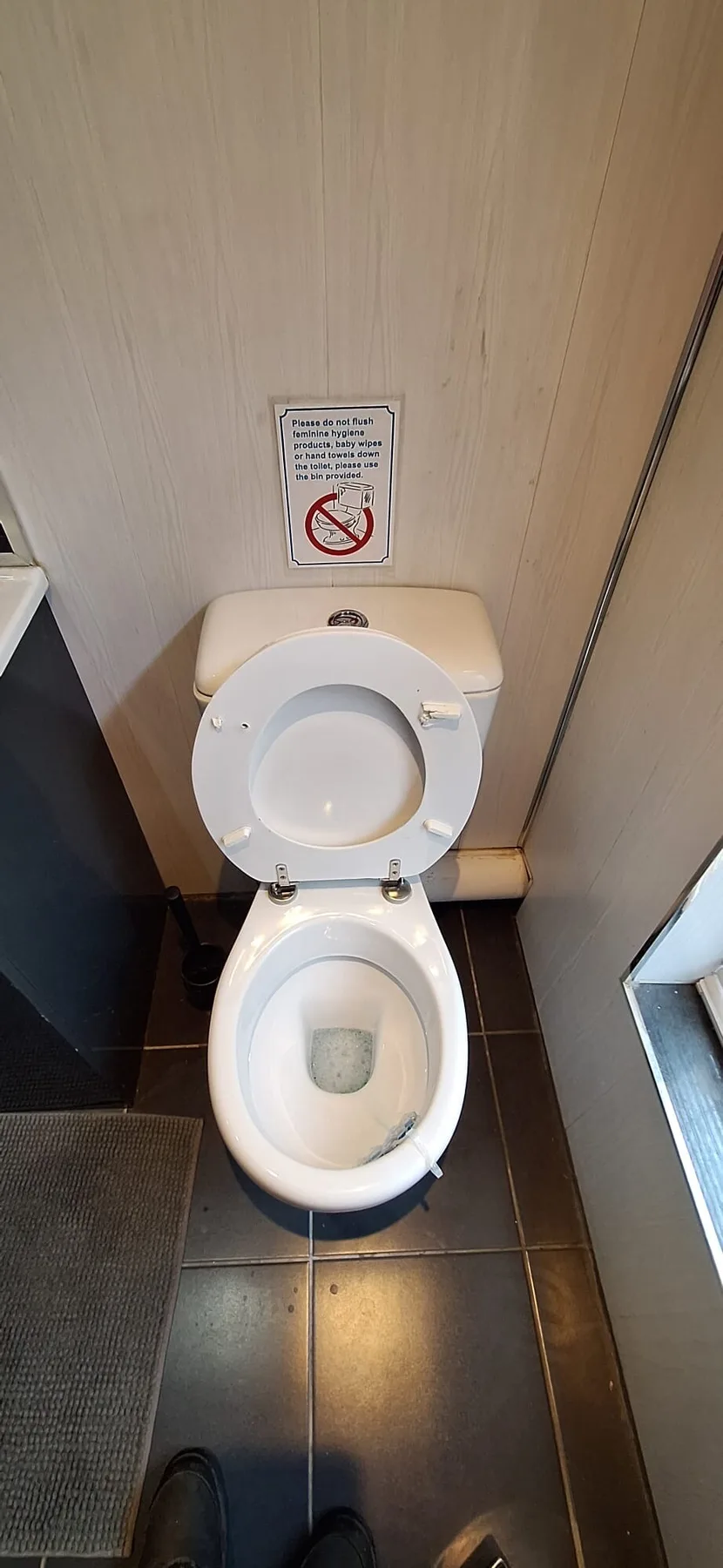 A toilet in a compact bathroom, with a small sign on the wall.