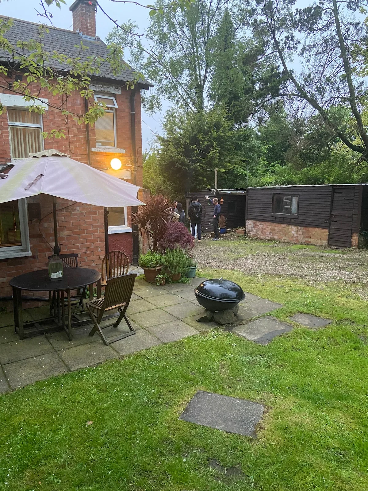 A garden patio beside a brick house, with outdoor seating and a grassy yard.
