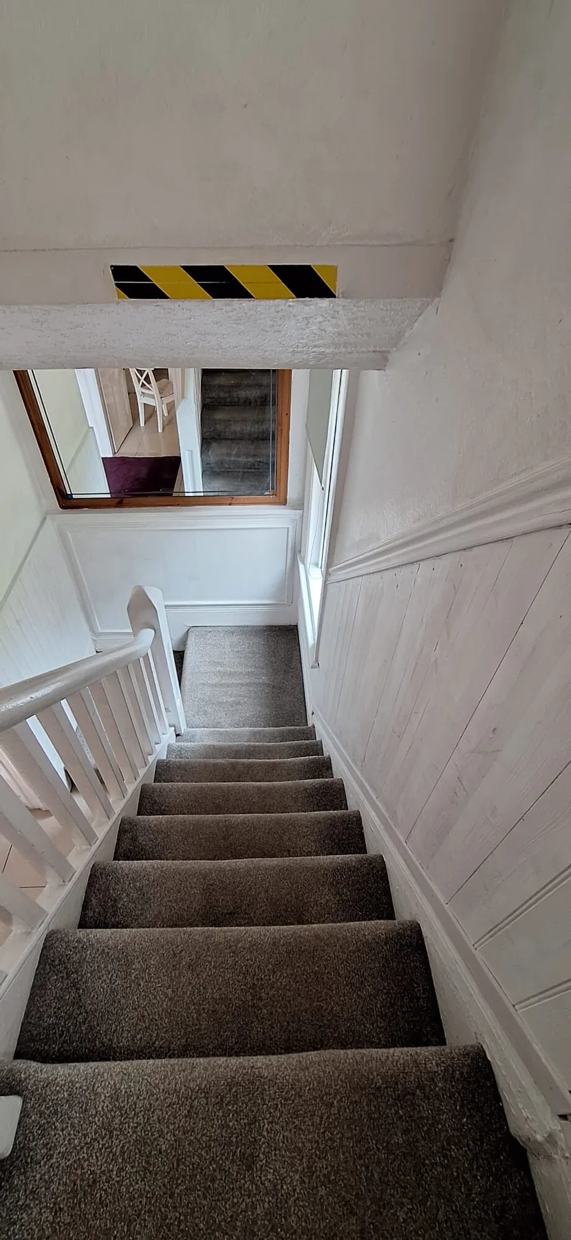 An indoor staircase with carpeted steps and white railings descends toward a window.