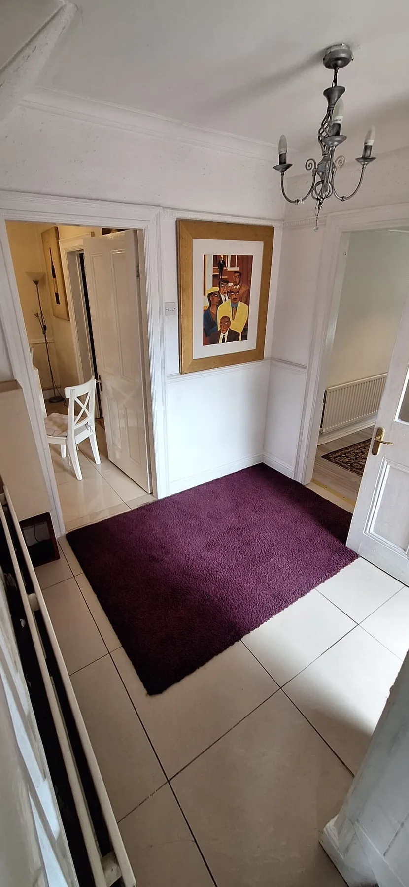 A tiled entry hall with a purple rug, framed artwork, and a chandelier.