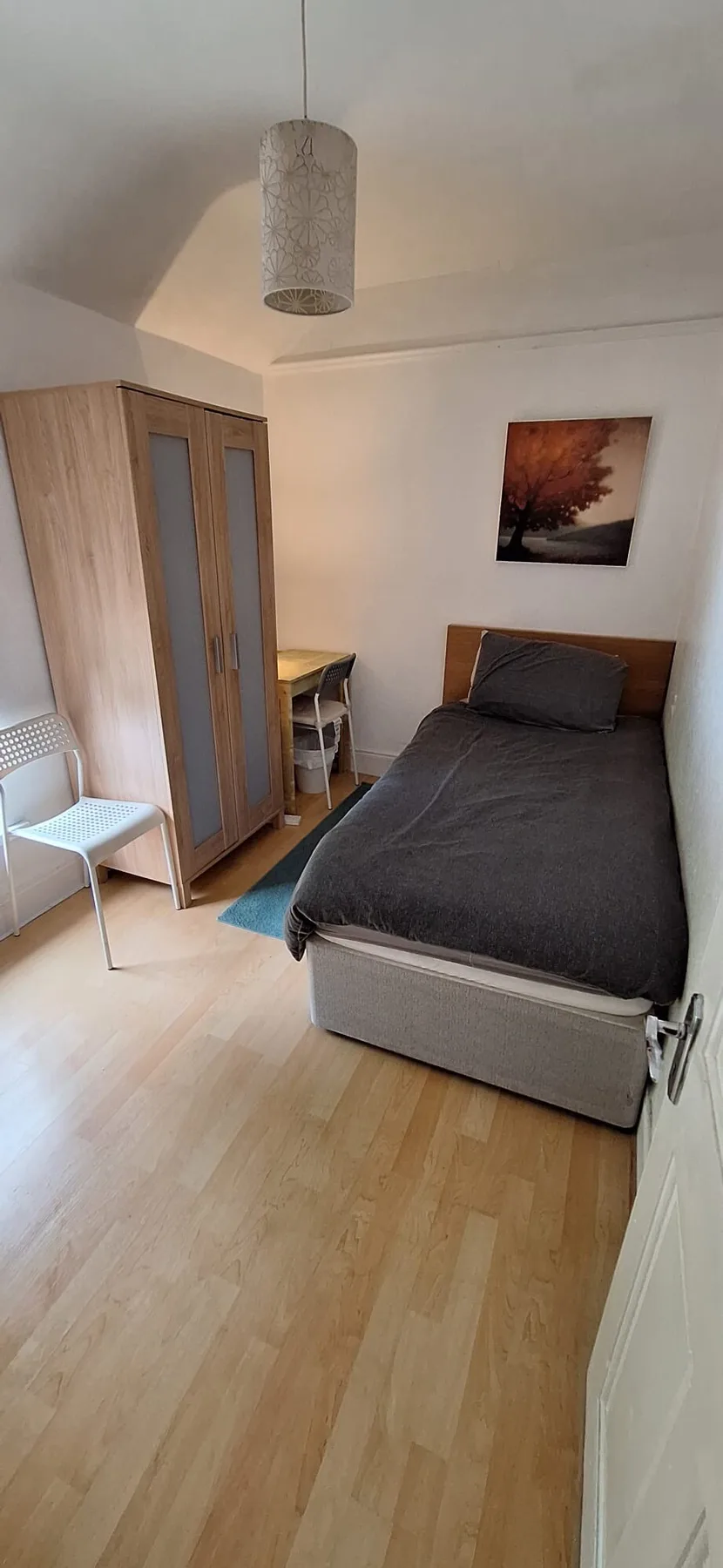 A bedroom with a single bed, wardrobe, and a white chair.