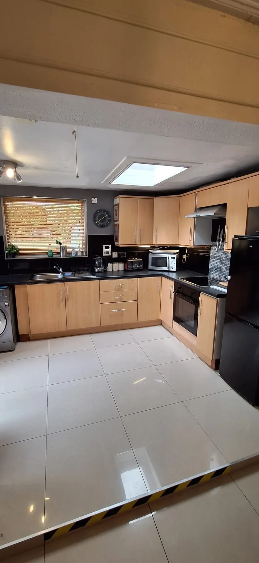 A kitchen with light wood cabinets, dark countertops, and a tiled floor.