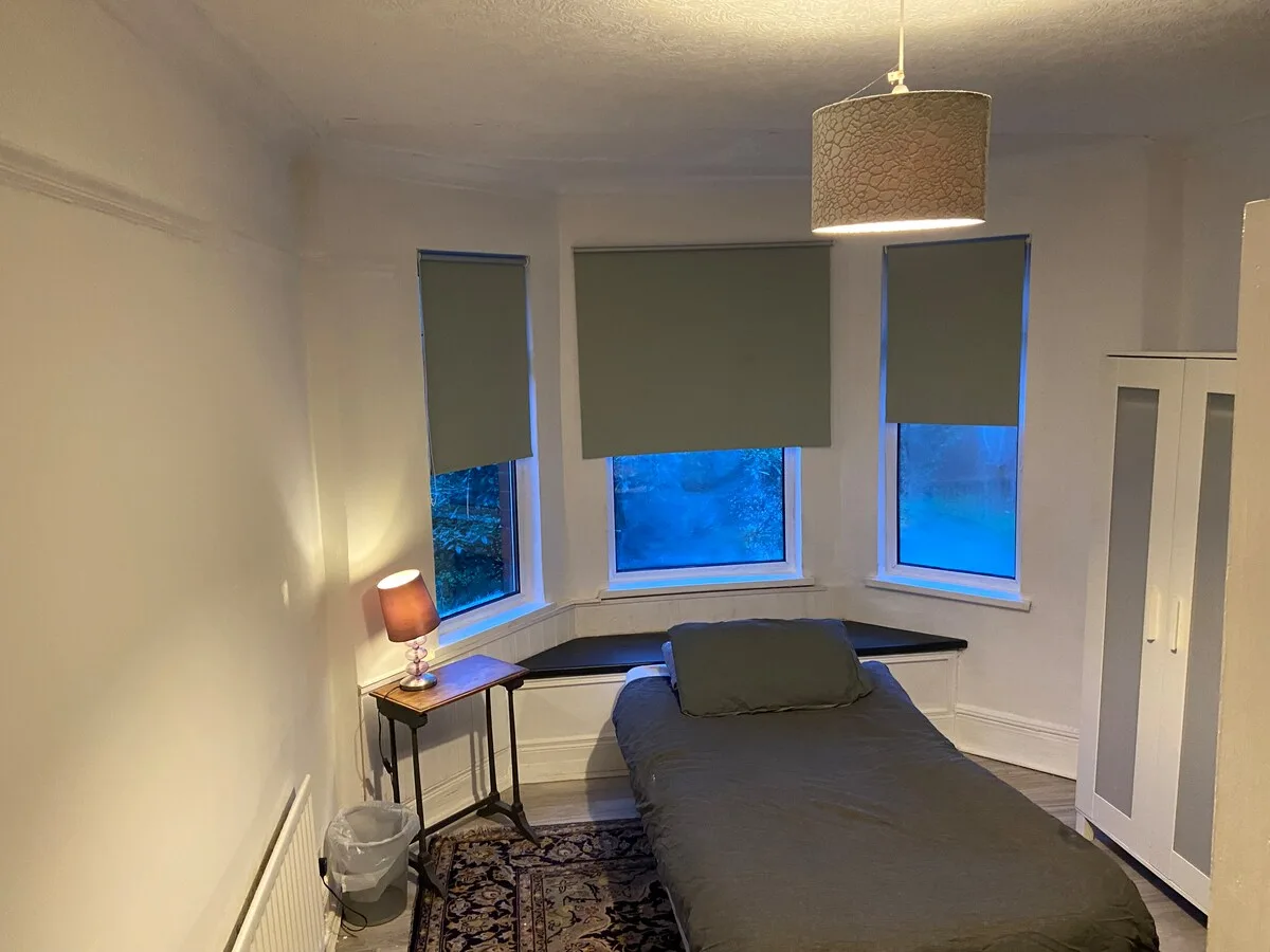 A bedroom with a bed beneath three windows with lowered blinds.