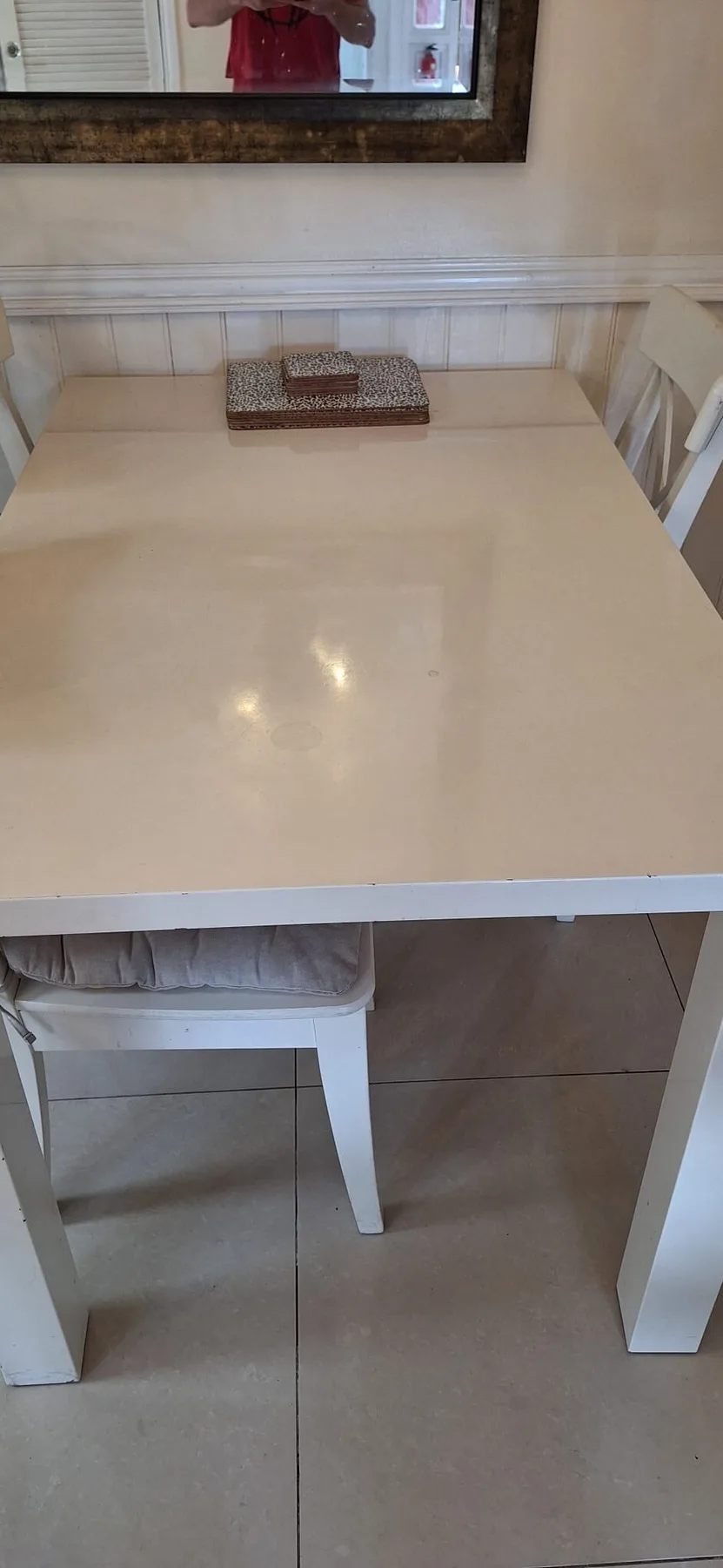 A small dining table with white seating stands against a paneled wall.