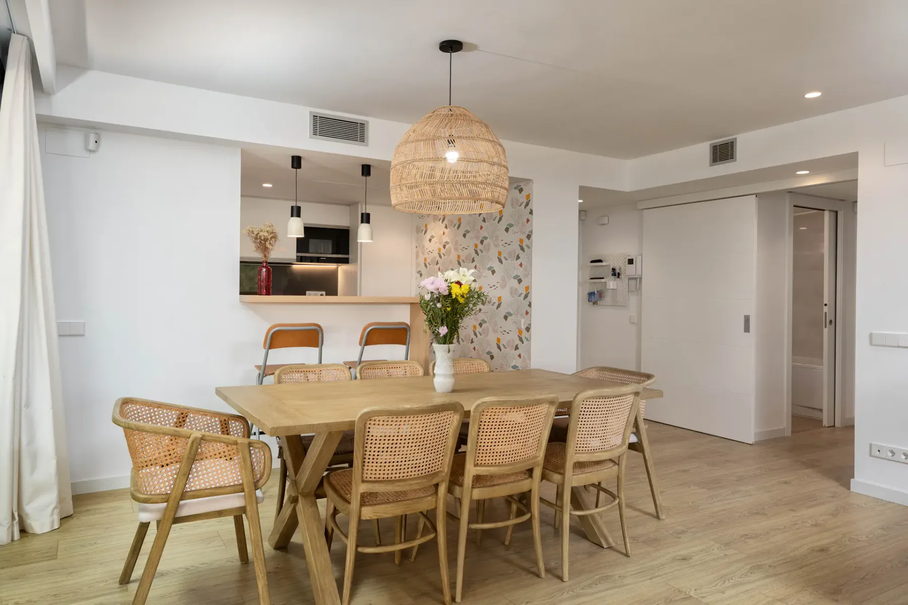 A dining area with a wooden table, woven chairs, and a hanging pendant light.