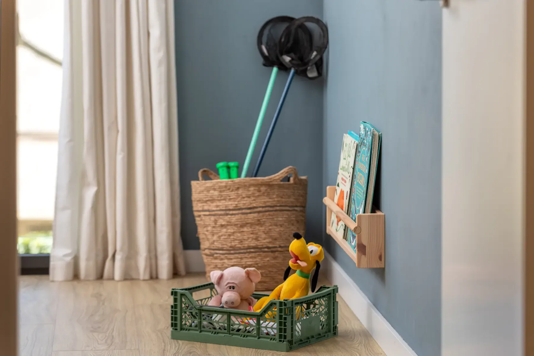 A play area with toys in a green crate beside a blue wall.