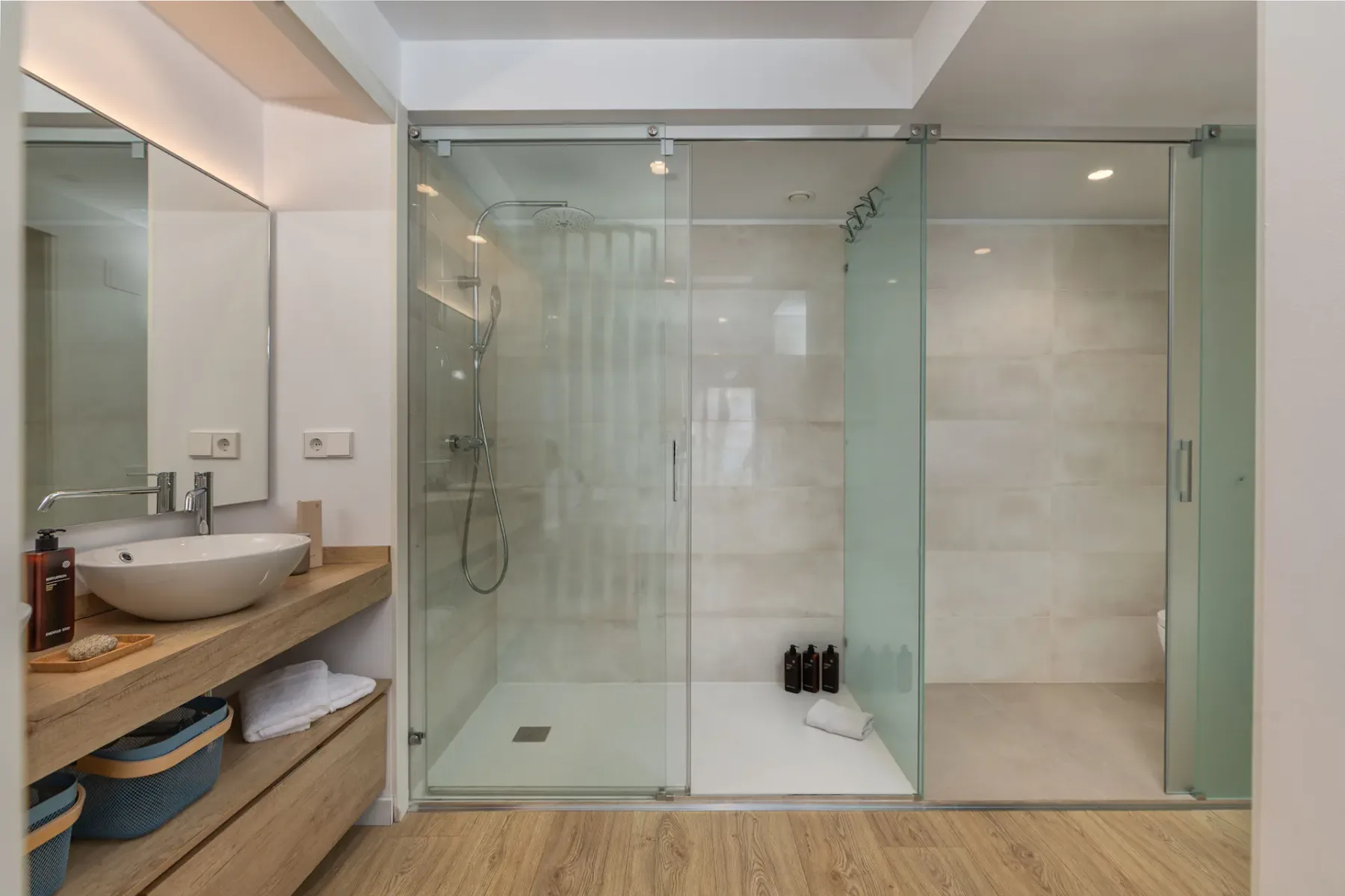 A bathroom with a glass-enclosed shower and a sink beside a wood vanity.