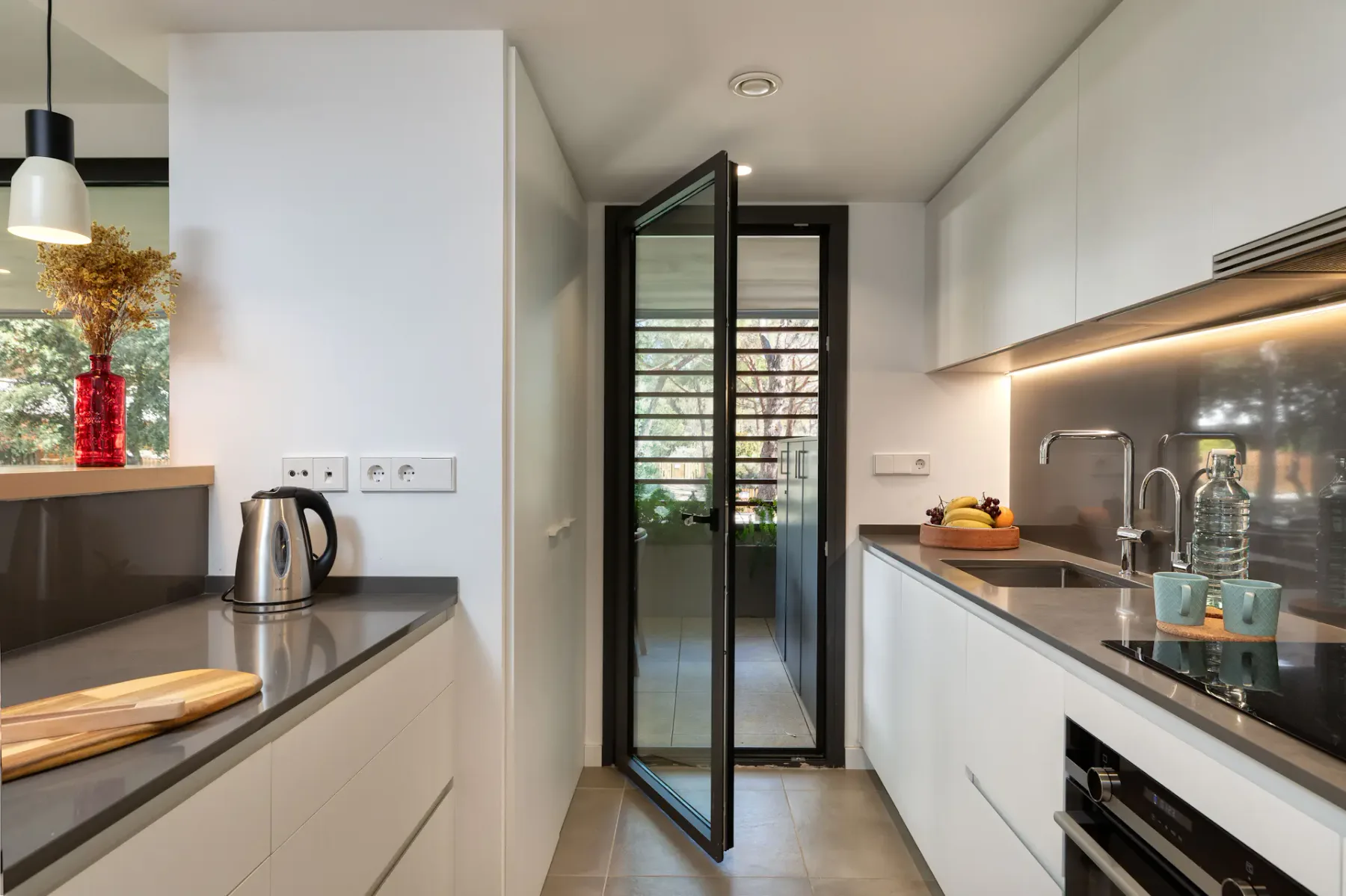 A modern kitchen with counters on both sides and a glass door at the far end.