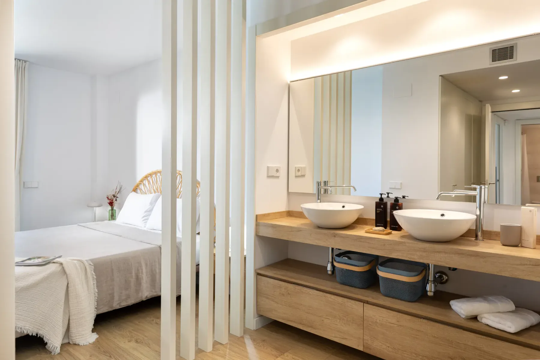 A bedroom beside a vanity area with two sinks and a large mirror.