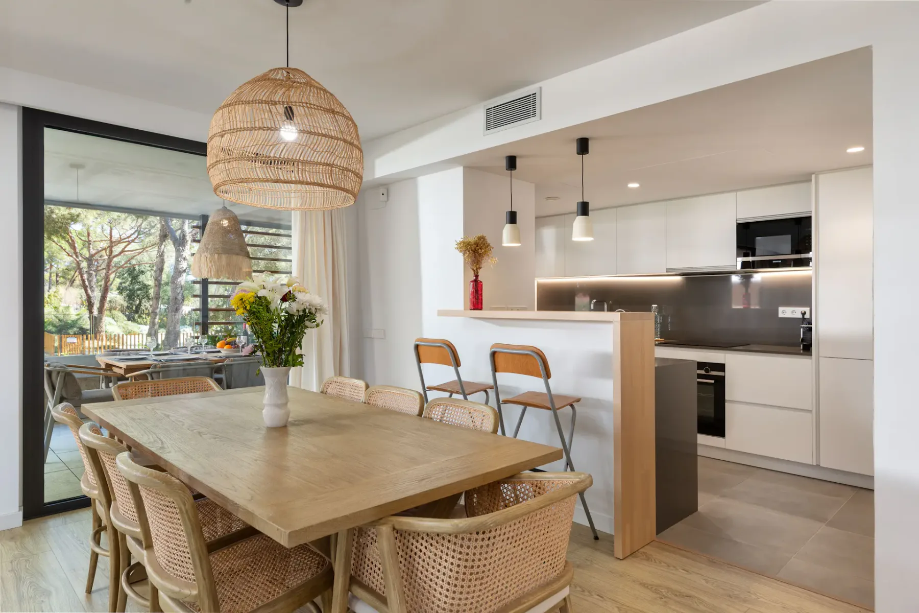 A dining area opens onto a bright kitchen, with a table beside glass doors.