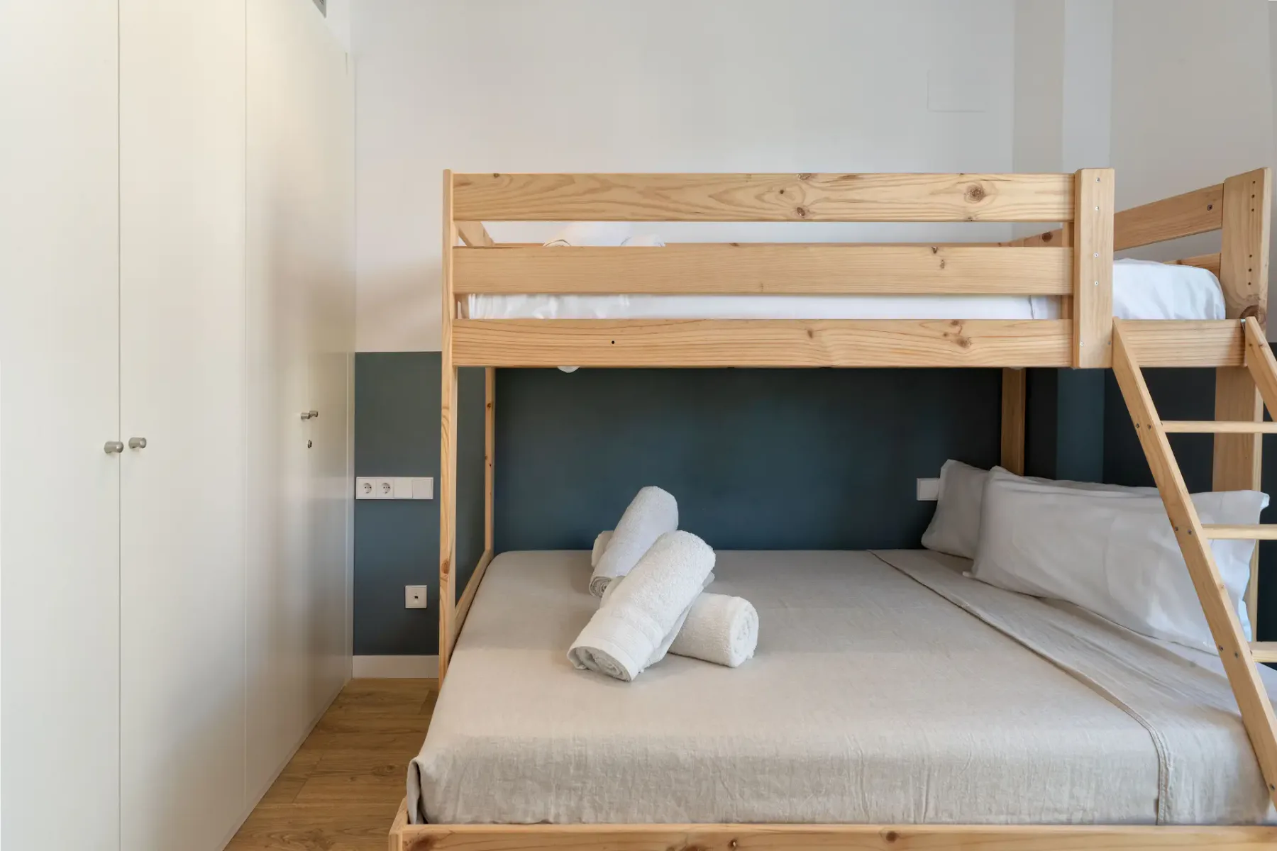 A bedroom with a wooden bunk bed and neatly arranged white bedding.