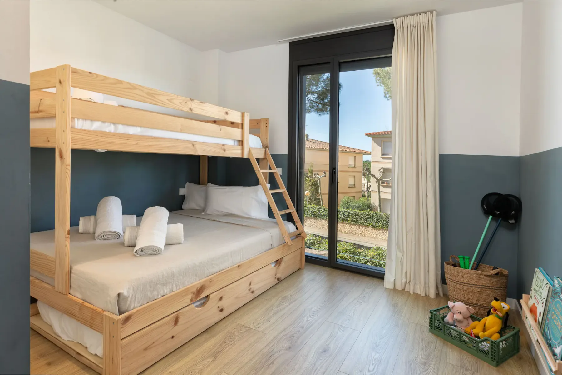 A bedroom with a wooden bunk bed beside a tall glass door and curtains.