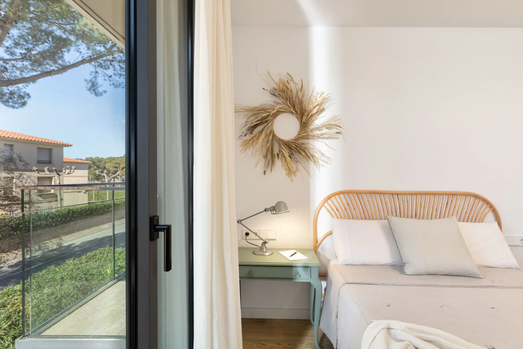 A bright bedroom with a bed beside a large glass door and bedside table.