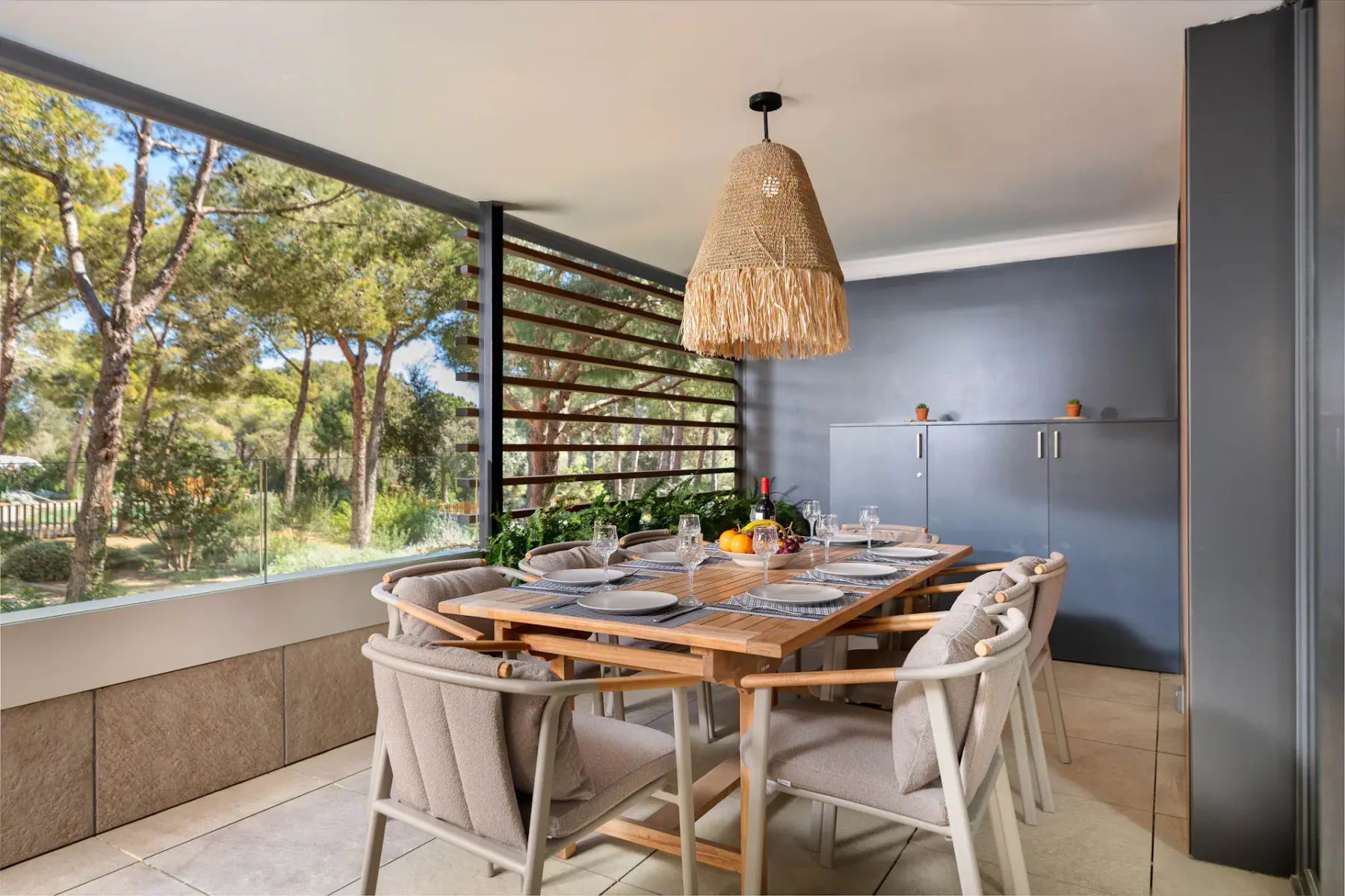 A dining area with a wooden table and large windows overlooking trees.