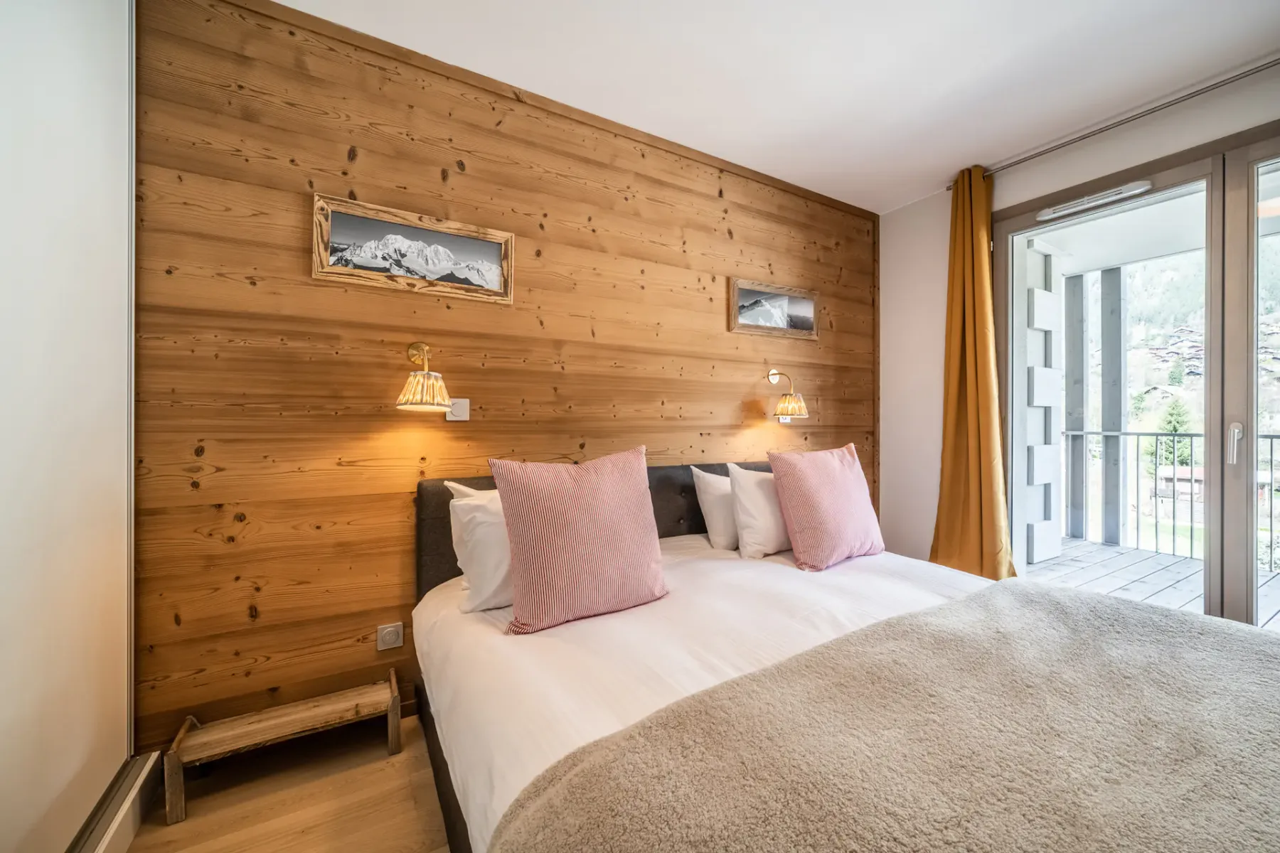 Un dormitorio con una cama junto a una pared revestida de madera y una puerta acristalada al balcón.