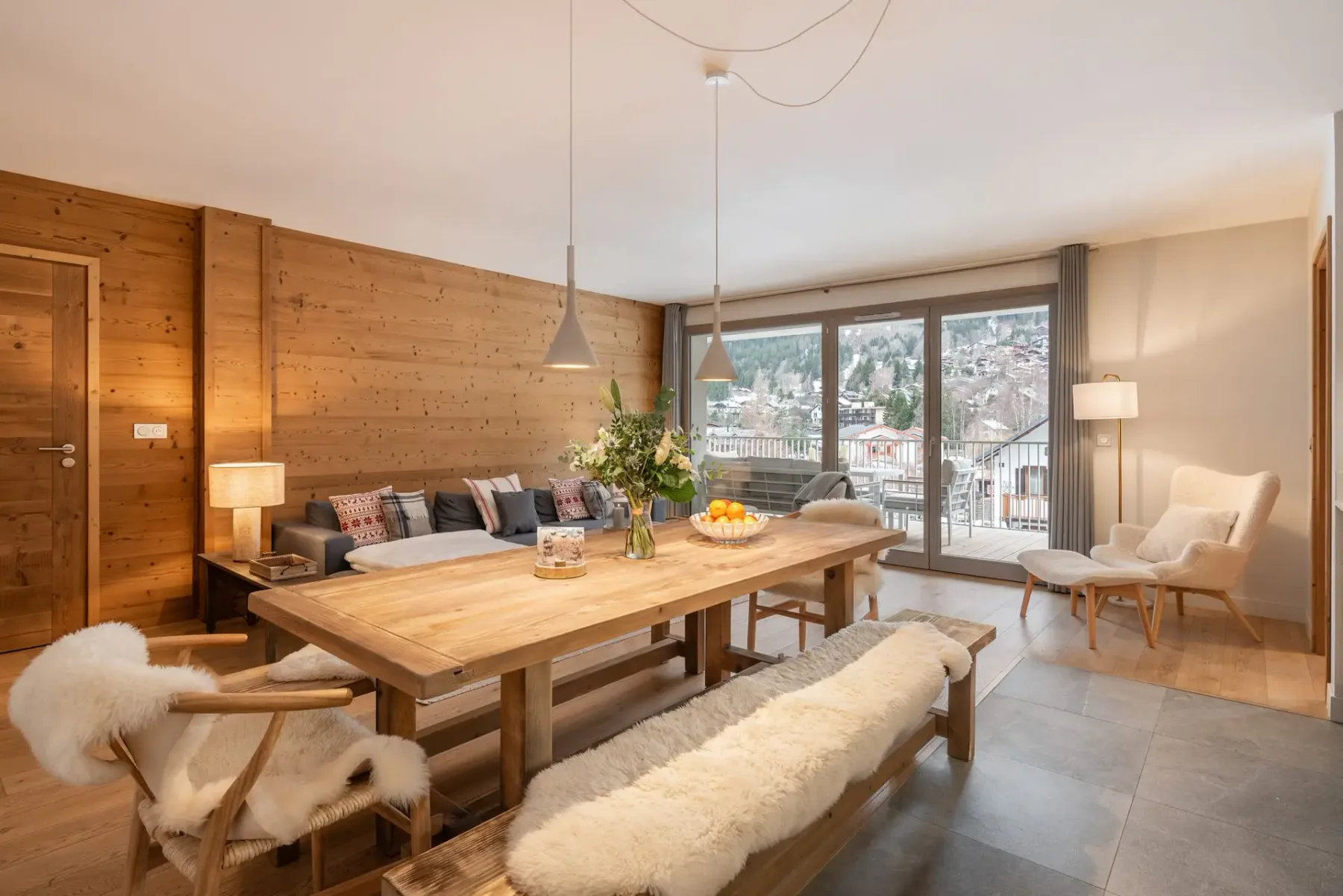 Una zona de comedor y estar cuenta con una mesa de madera y grandes ventanales con vistas al pueblo.