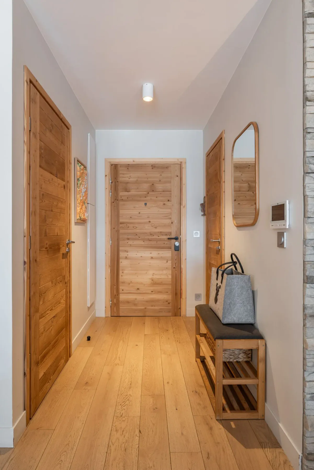 Un pasillo con puertas de madera y un banco debajo de un espejo.