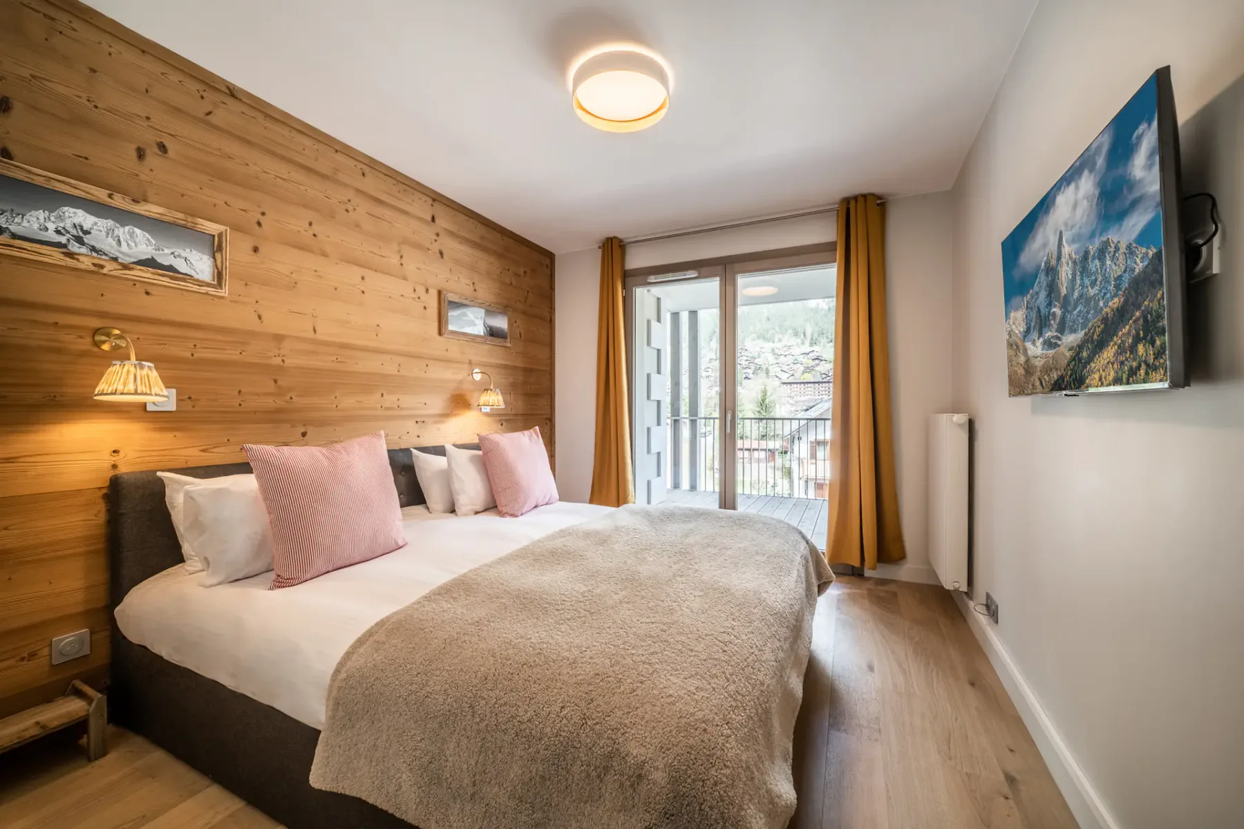 Un dormitorio con una cama, una pared revestida de madera y puertas de vidrio hacia un balcón.