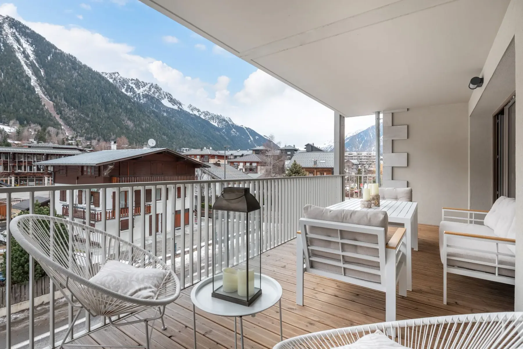 Un balcón amueblado con asientos mira hacia un pueblo de montaña y picos nevados.
