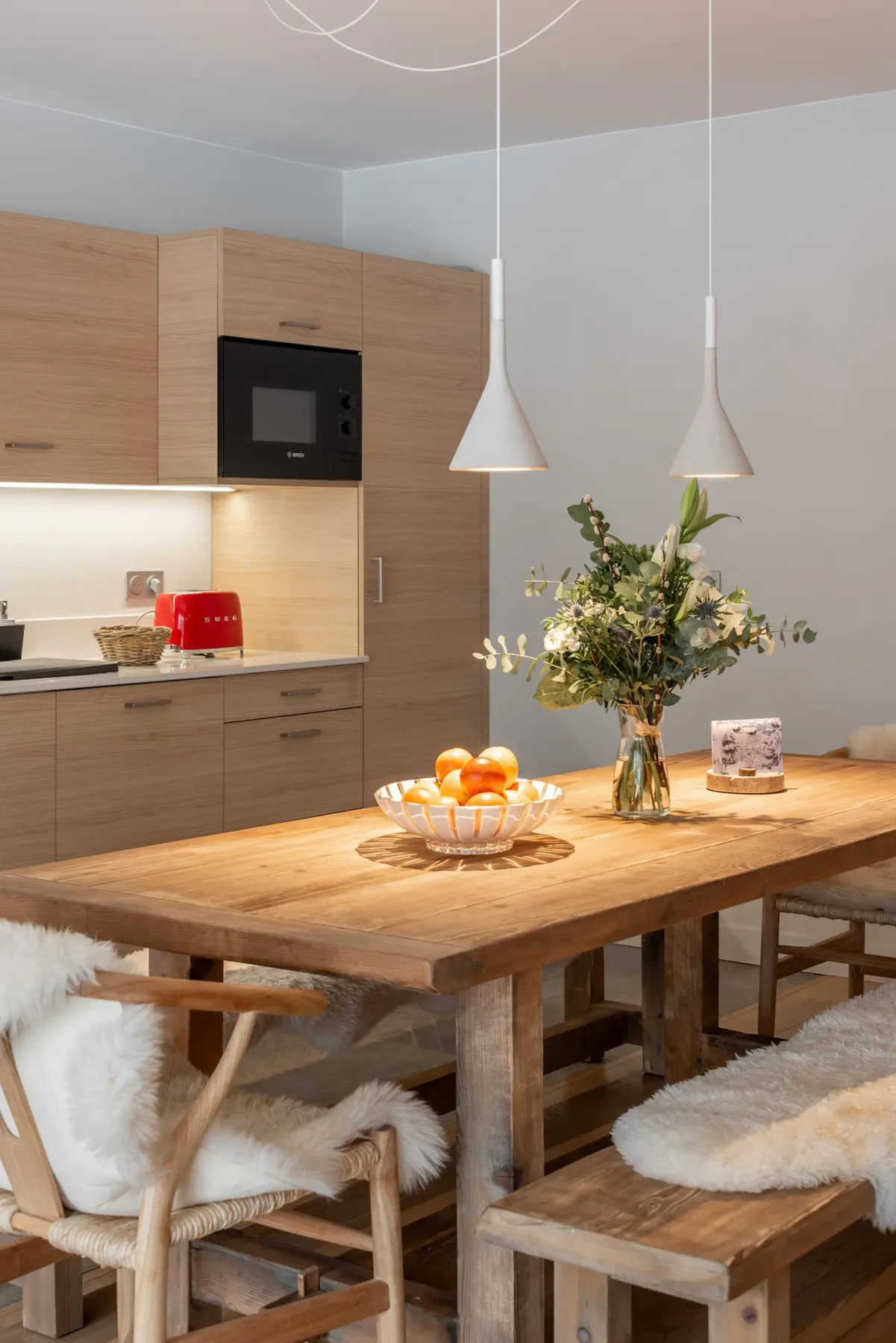 Comedor con mesa de madera, asientos y cocina abierta.