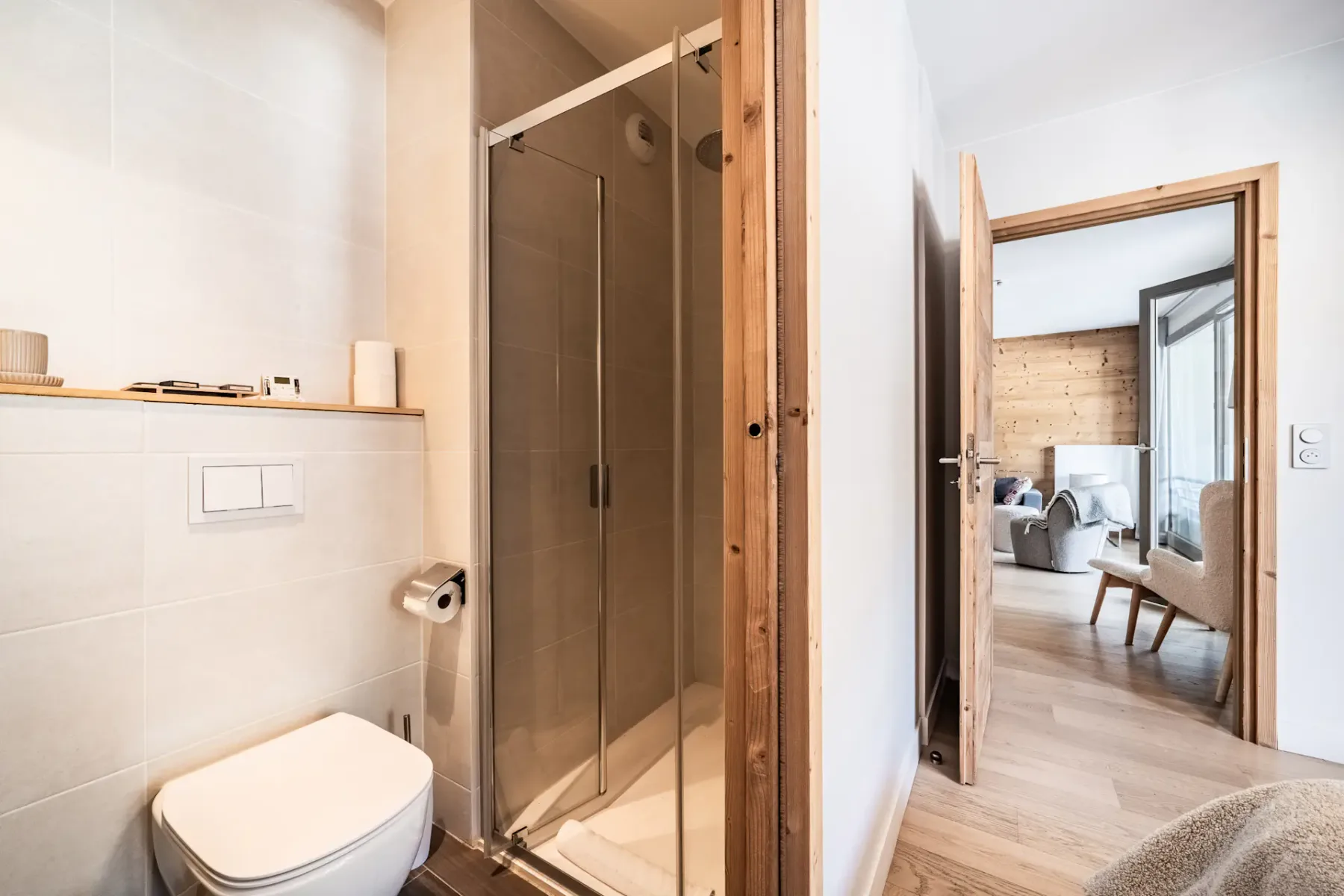 Un baño con ducha de vidrio e inodoro, abierto a una zona de estar.