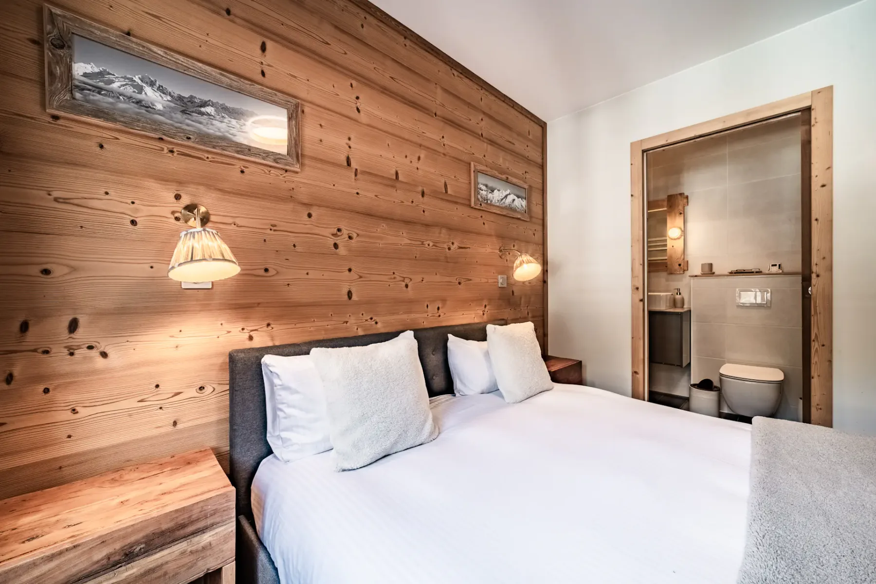 Un dormitorio con una cama bien tendida junto a una pared revestida de madera.