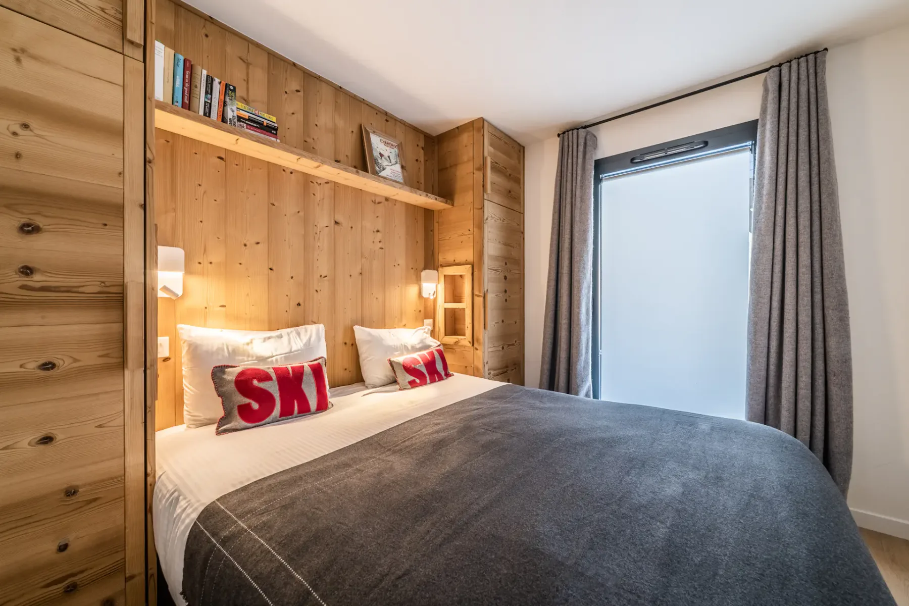 Un dormitorio con una cama, paredes revestidas de madera y una gran ventana con cortinas.