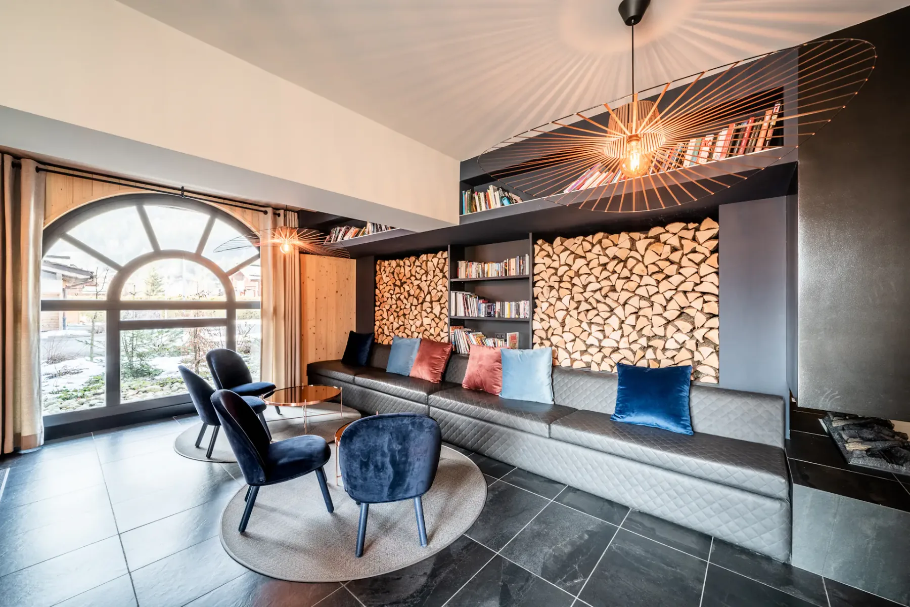 Un salón con un sofá largo, asientos oscuros y una gran ventana arqueada.