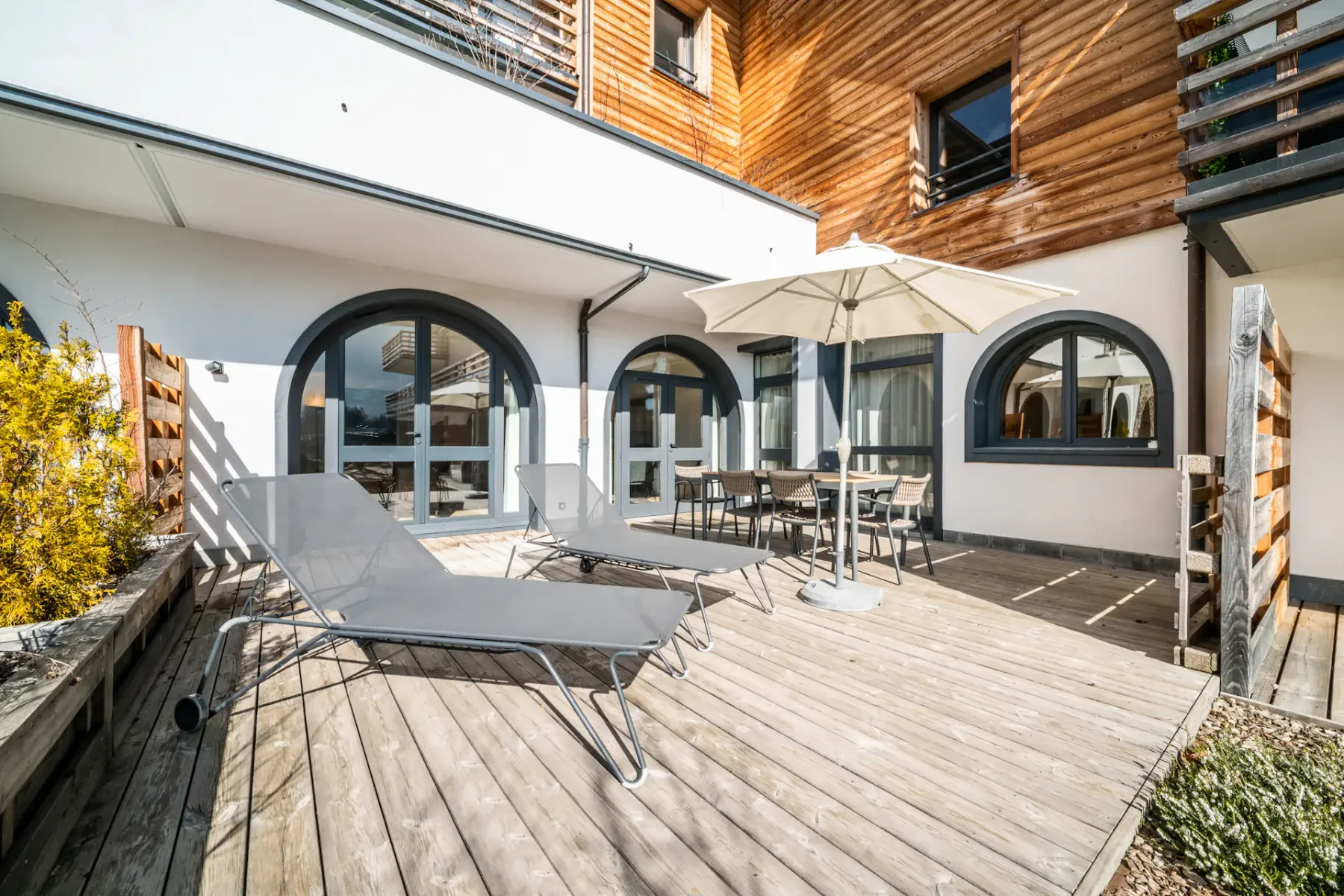 Una terraza de madera con asientos de exterior y una sombrilla junto a un edificio moderno.