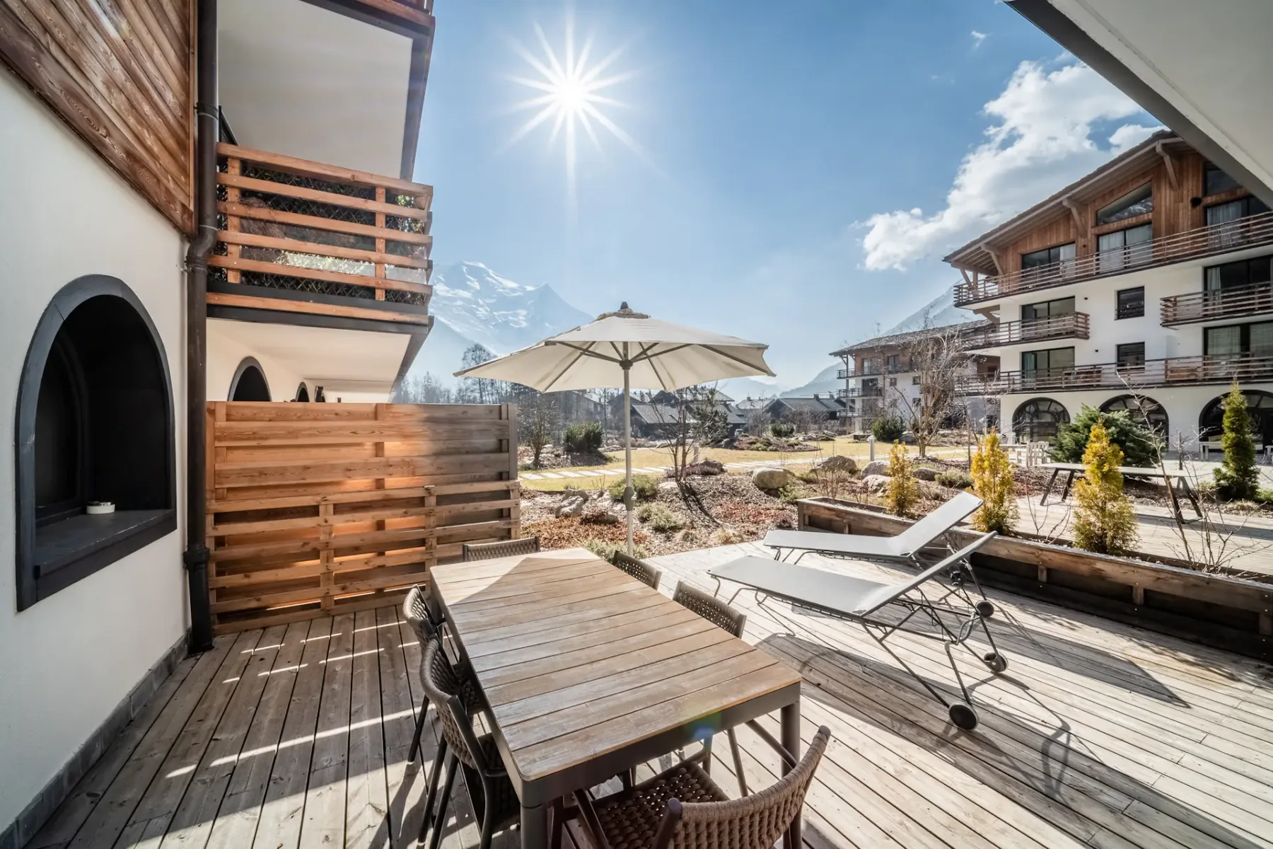 Una terraza soleada al aire libre con una mesa de madera, asientos y una sombrilla abierta.