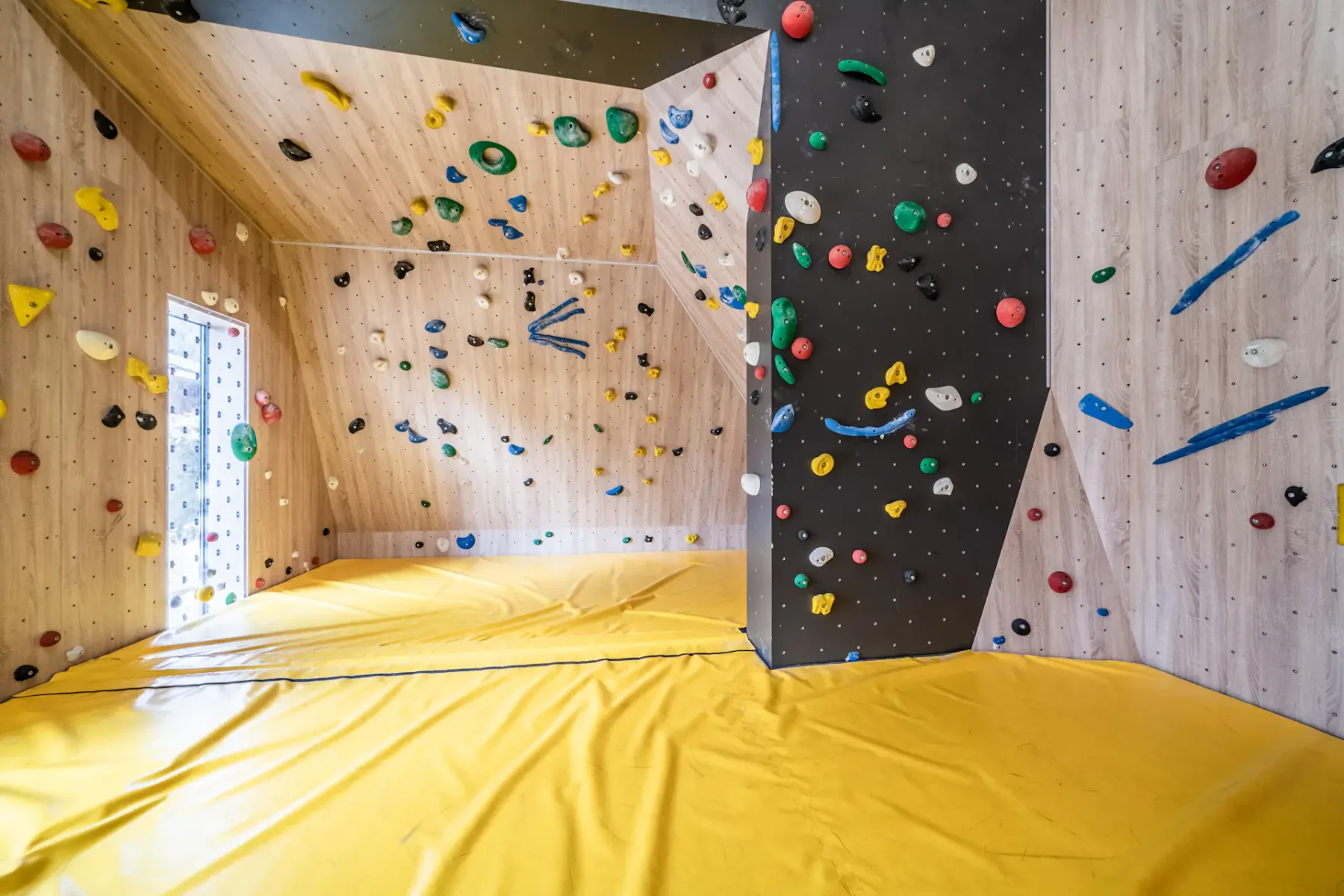 Una pared de escalada interior con presas de colores sobre un suelo acolchado.
