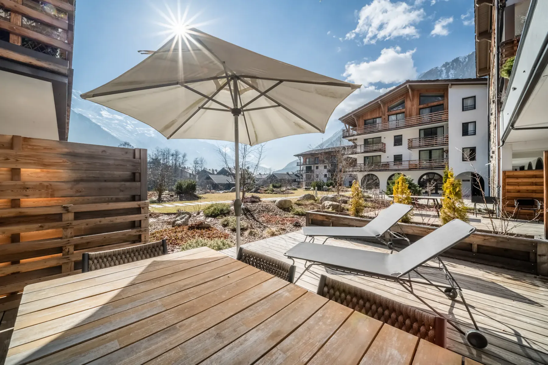 Una terraza soleada al aire libre tiene asientos reclinables bajo una gran sombrilla.