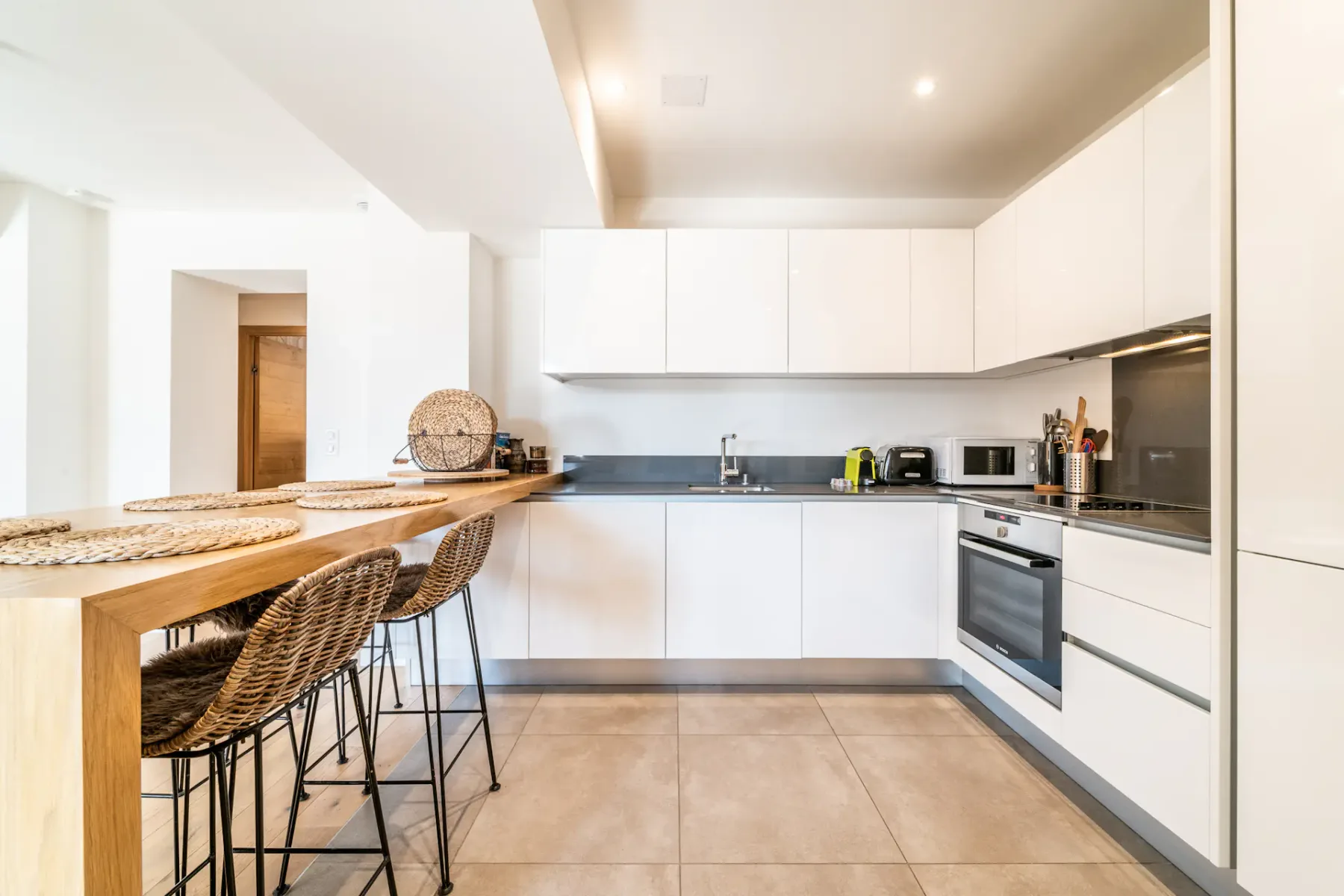 Una cocina moderna y luminosa con armarios blancos y una barra de madera.