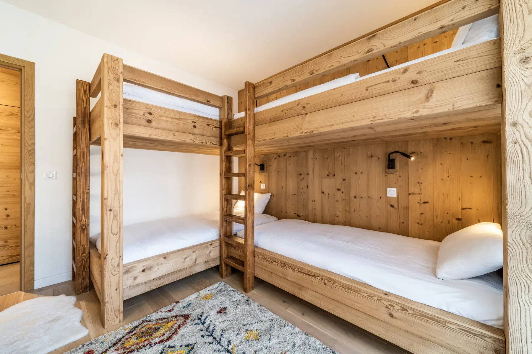 Un dormitorio con literas de madera, ropa de cama blanca y una alfombra estampada.