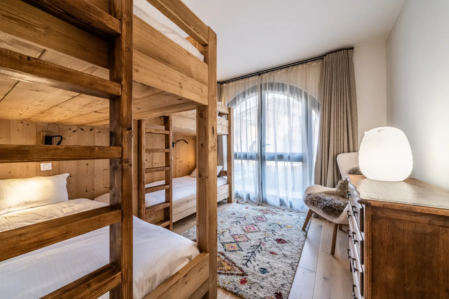 Un dormitorio con literas de madera, una ventana amplia y una alfombra estampada.