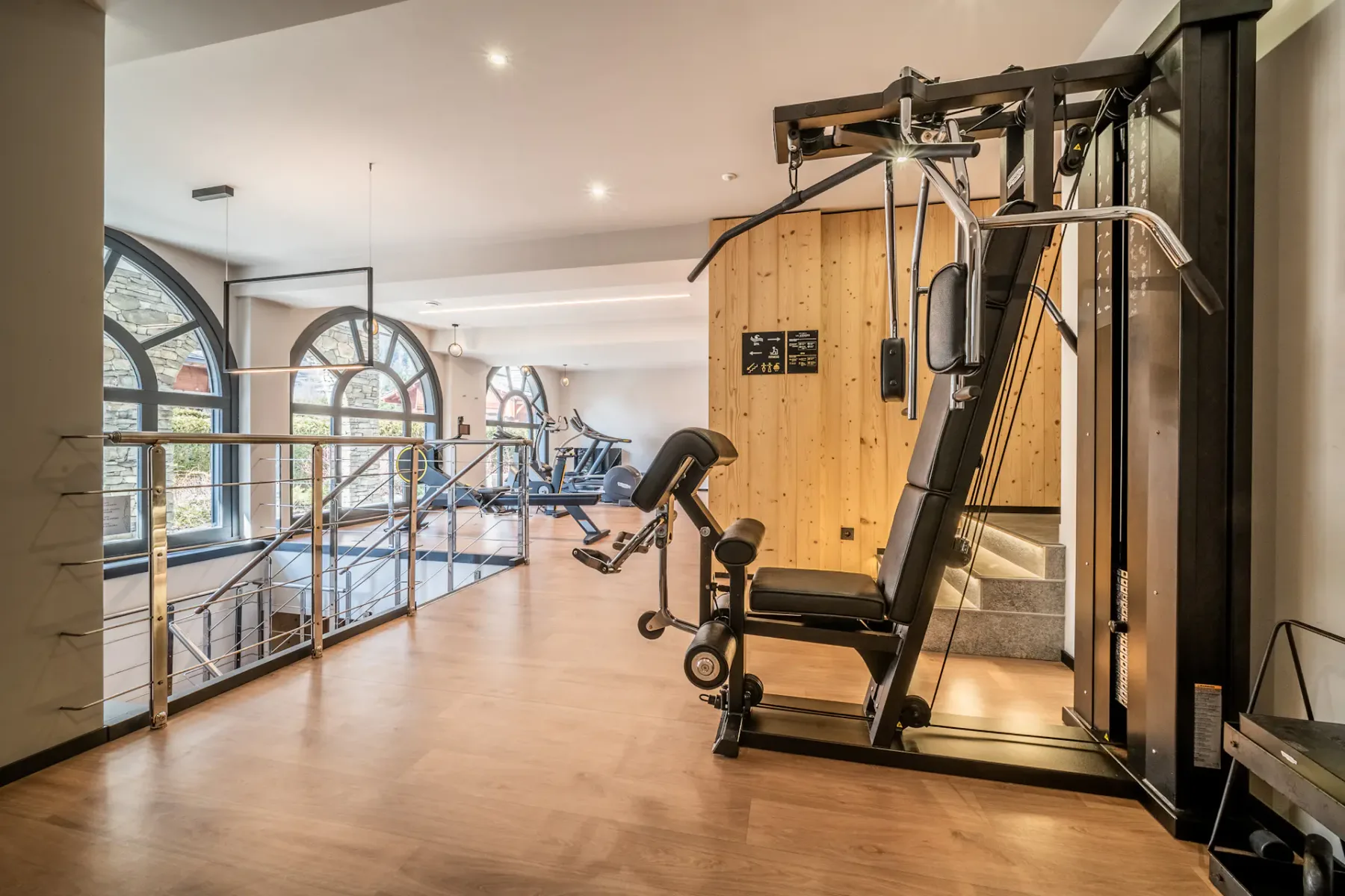Un gimnasio con máquinas de ejercicio junto a grandes ventanas arqueadas.
