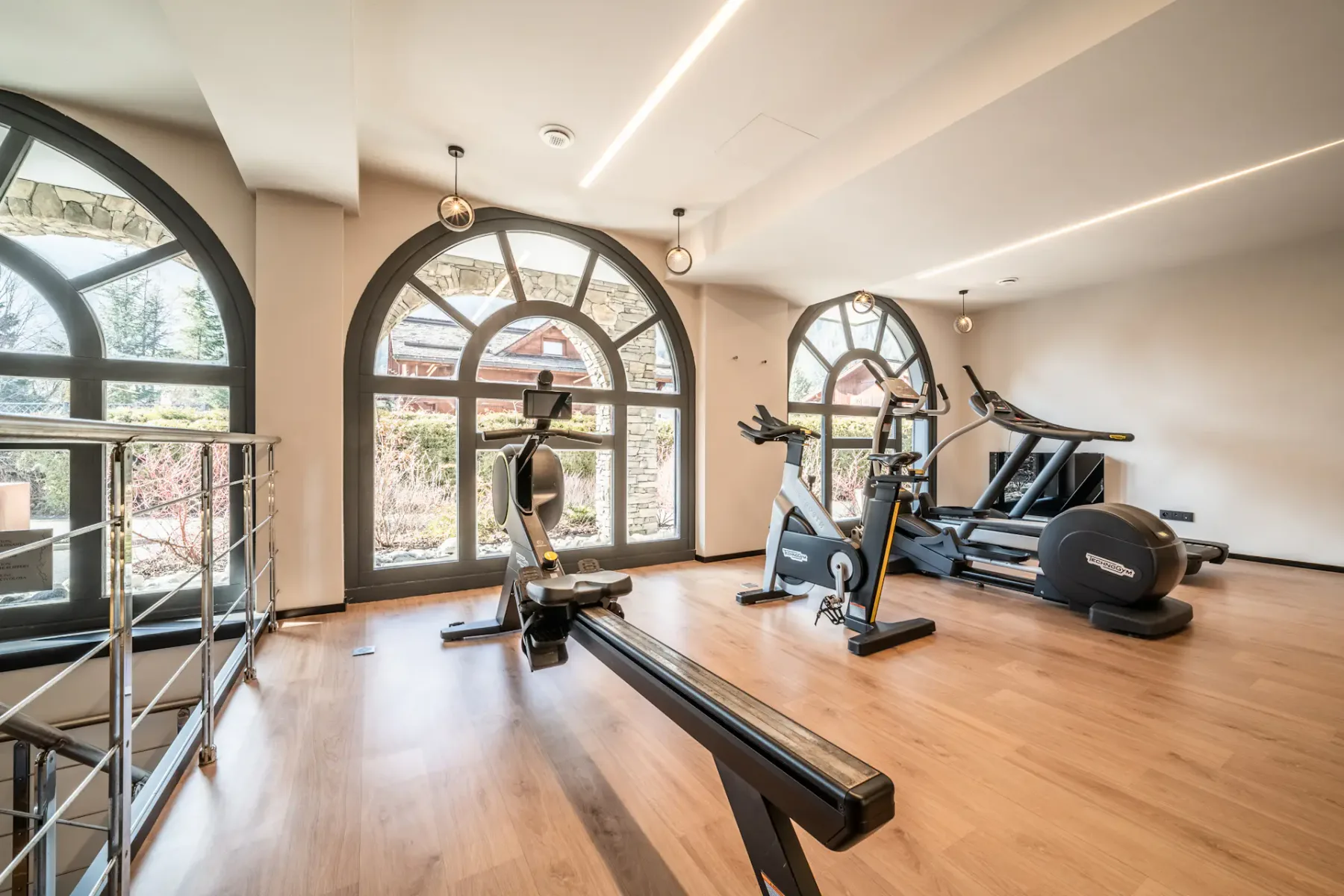 Un gimnasio luminoso con equipos de ejercicio y grandes ventanas arqueadas.