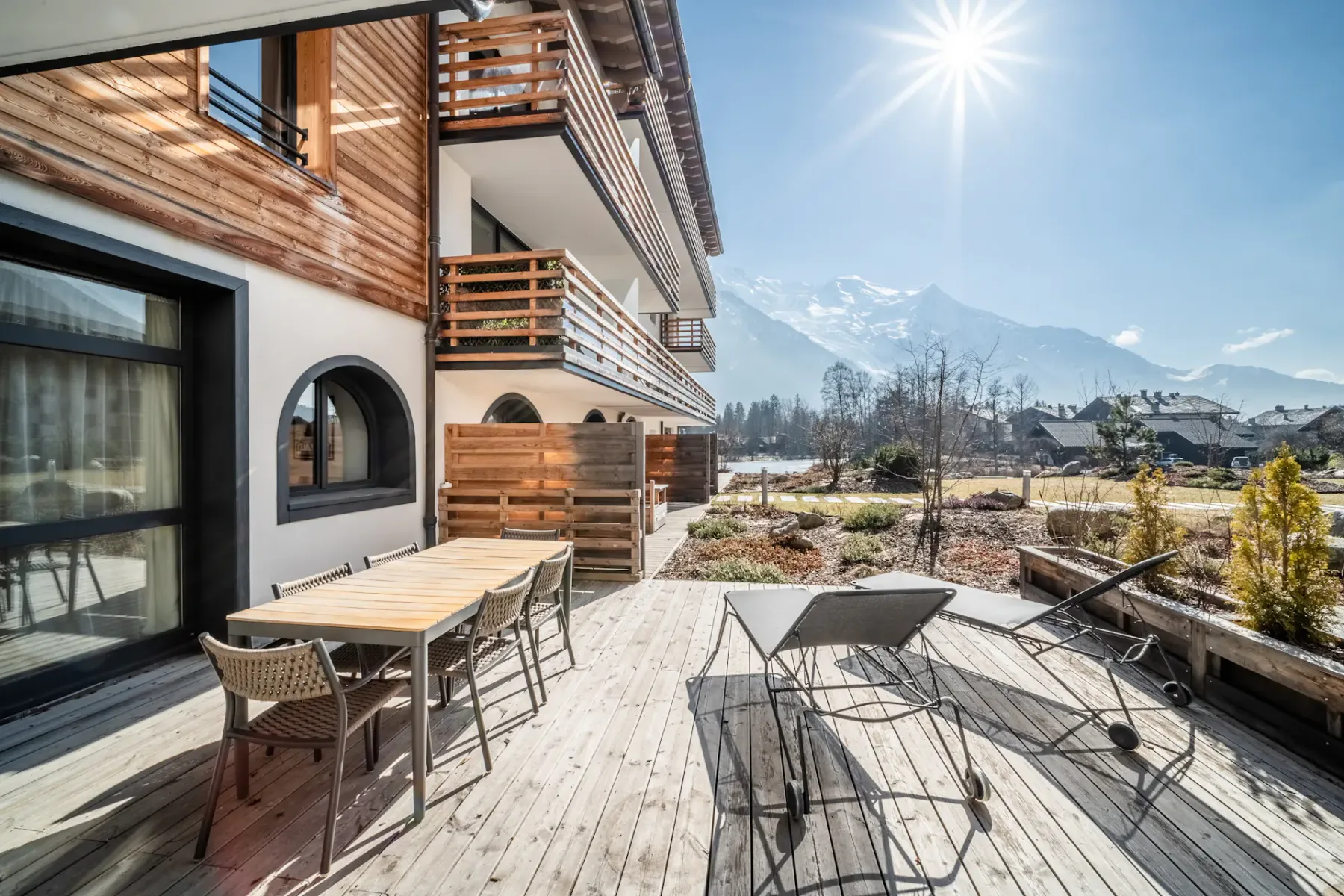 Una terraza exterior soleada junto a un edificio revestido de madera ofrece vistas a las montañas.